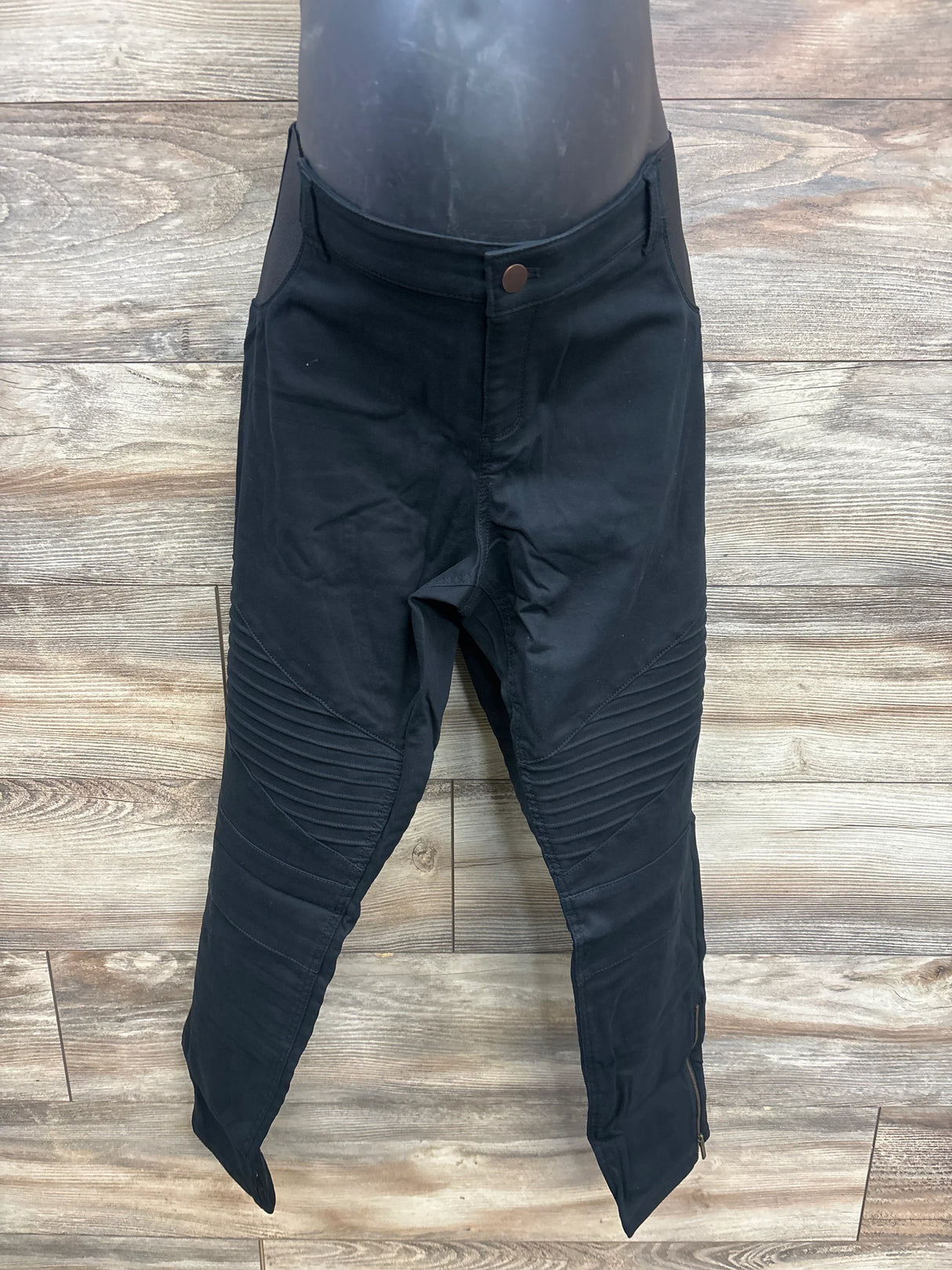 Front view of black maternity jeggings with ribbed knee panels, ankle zippers, and over-belly stretch panel on wood background