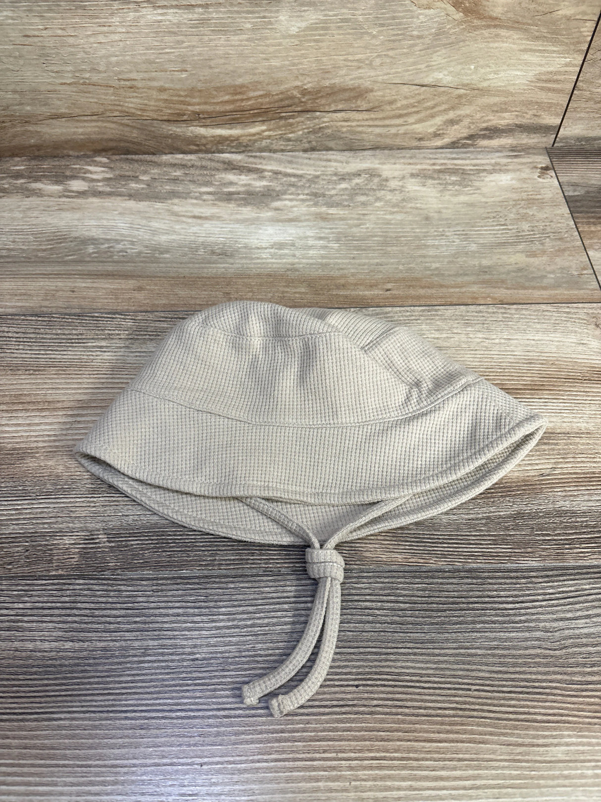 Top down view of baby waffle knit bucket hat beige showing textured waffle fabric and knotted chin ties on wood background