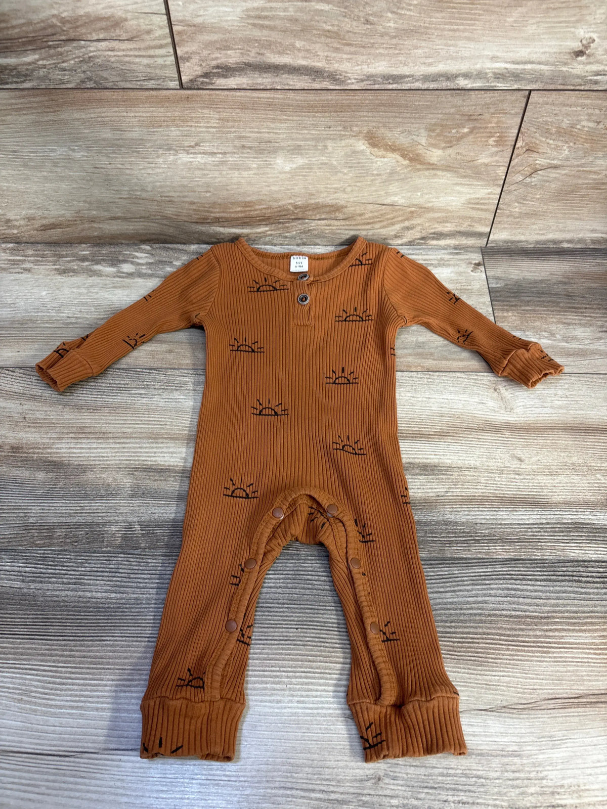 Flat lay of brown ribbed Henley baby coverall size 6 to 9 months showing front buttons, snap crotch and small sunrise print on wood background