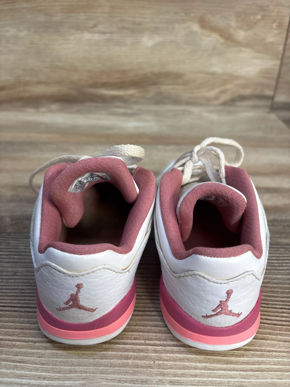 Back view of toddler white and pink athletic sneakers with Jumpman logo on wood floor