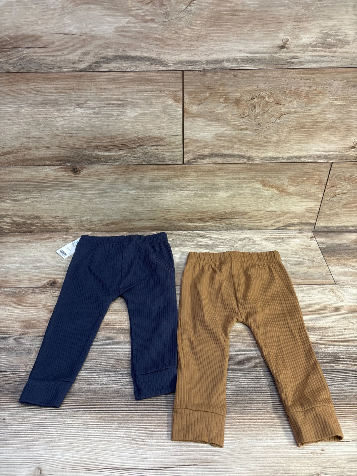 Front view of two Carter's ribbed baby pants navy and brown with elastic waistbands and cuffed ankles on wood background