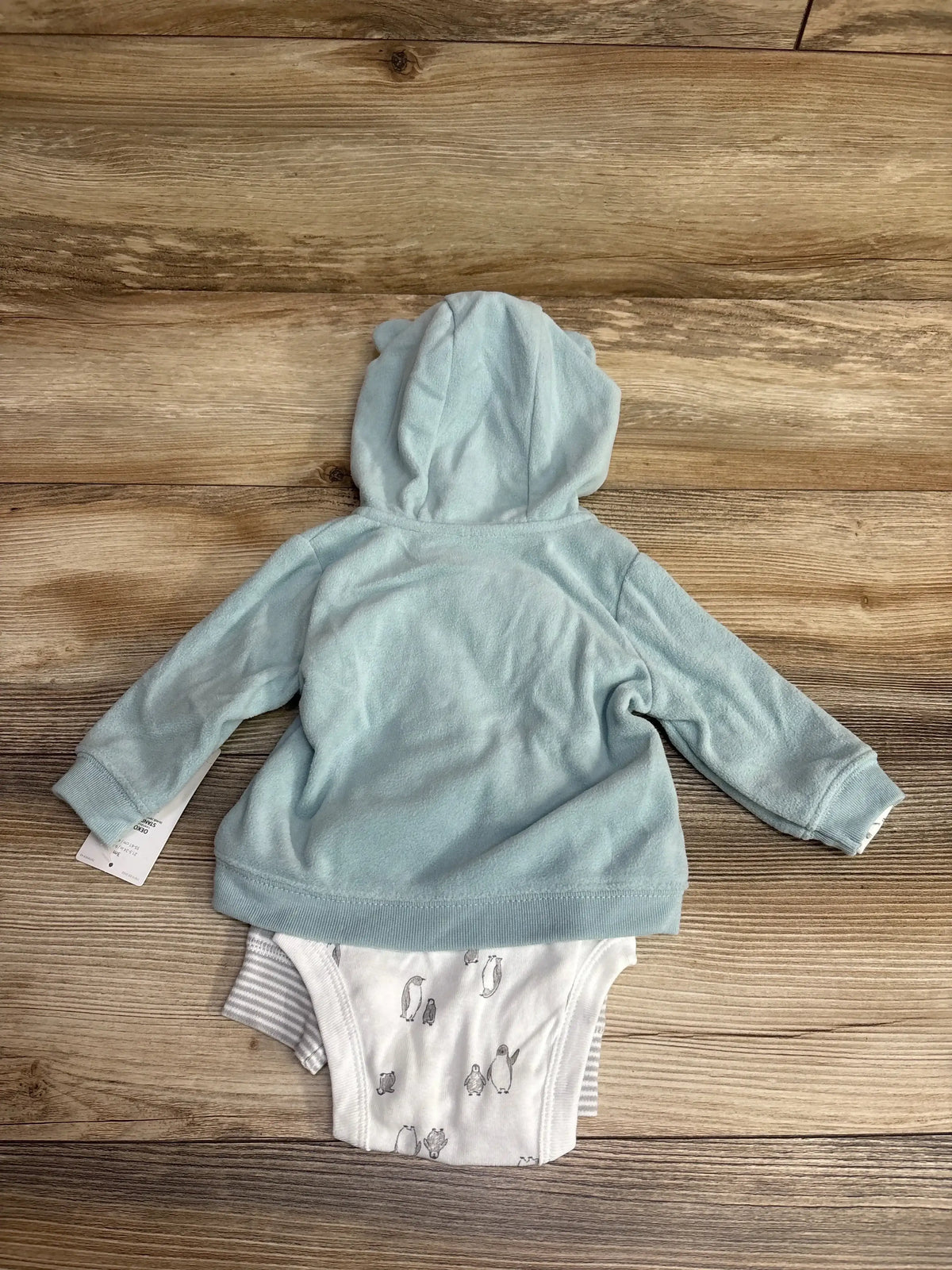 Light blue baby hoodie with ear details and printed onesie on wooden background