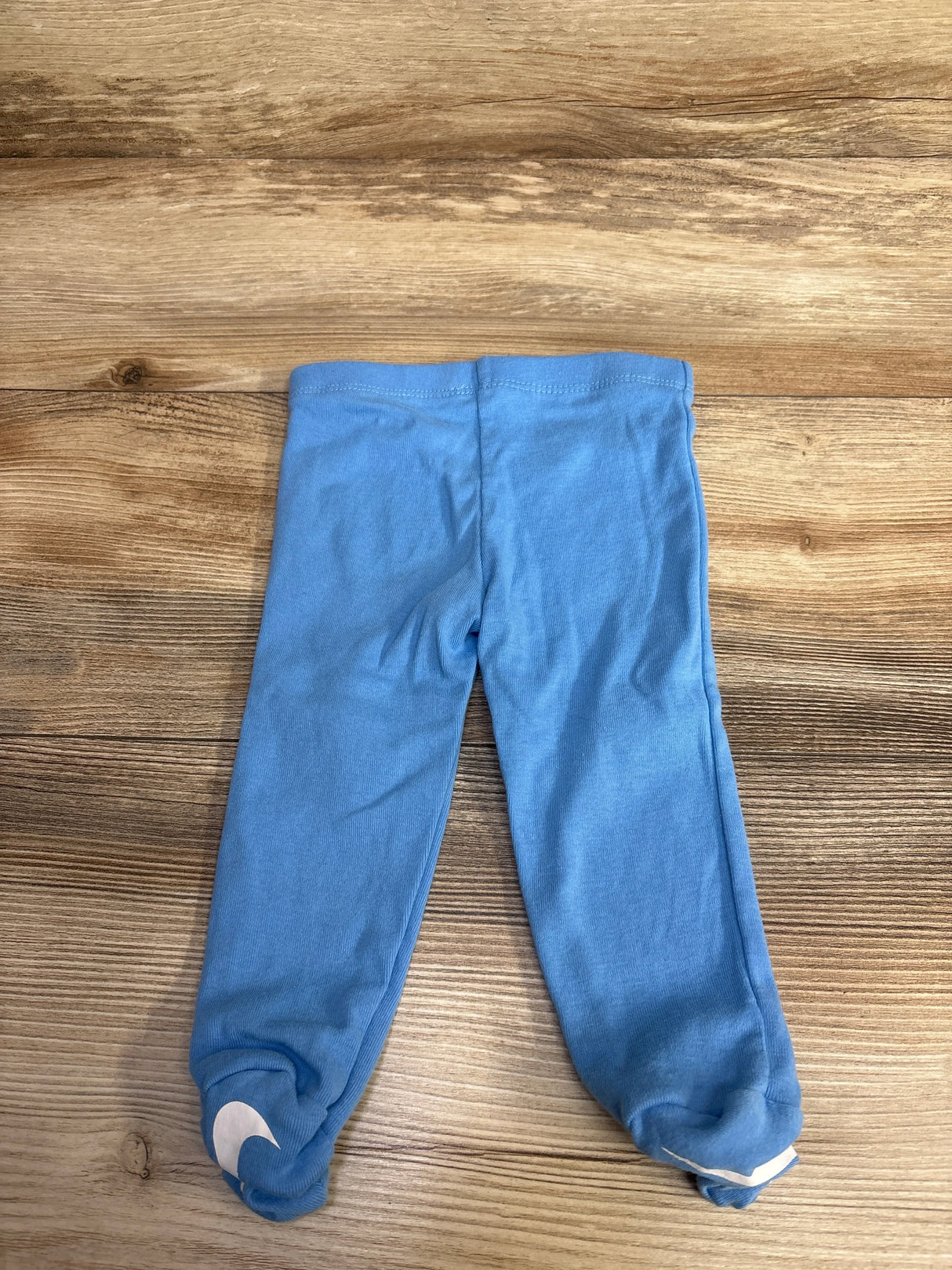 Light blue toddler leggings with Nike logo on feet, laid flat on wood floor