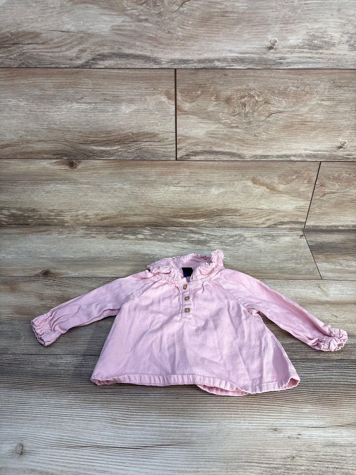 Front view of Baby Gap denim henley top in pink, showcasing ruffled collar, cuffs, and henley buttons on wood background