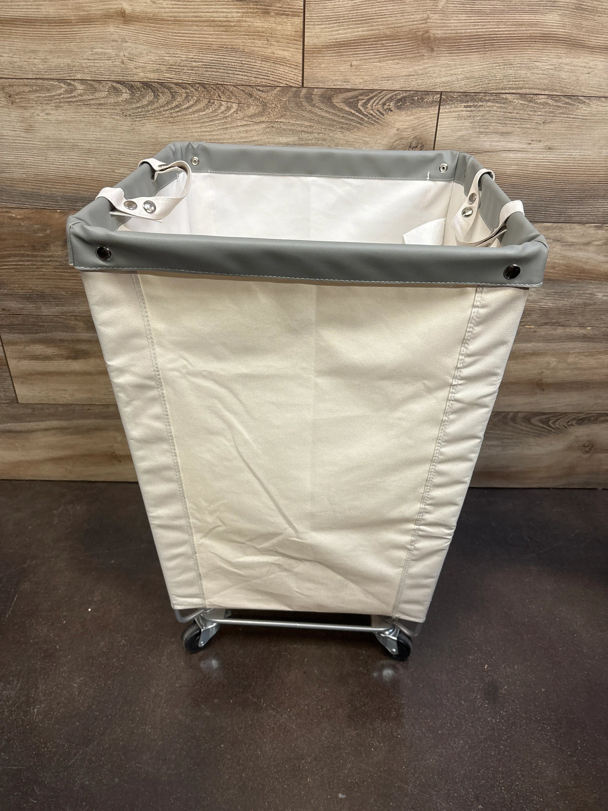 Front view of Seville Classics rolling laundry hamper with natural canvas and gray rim on wood background