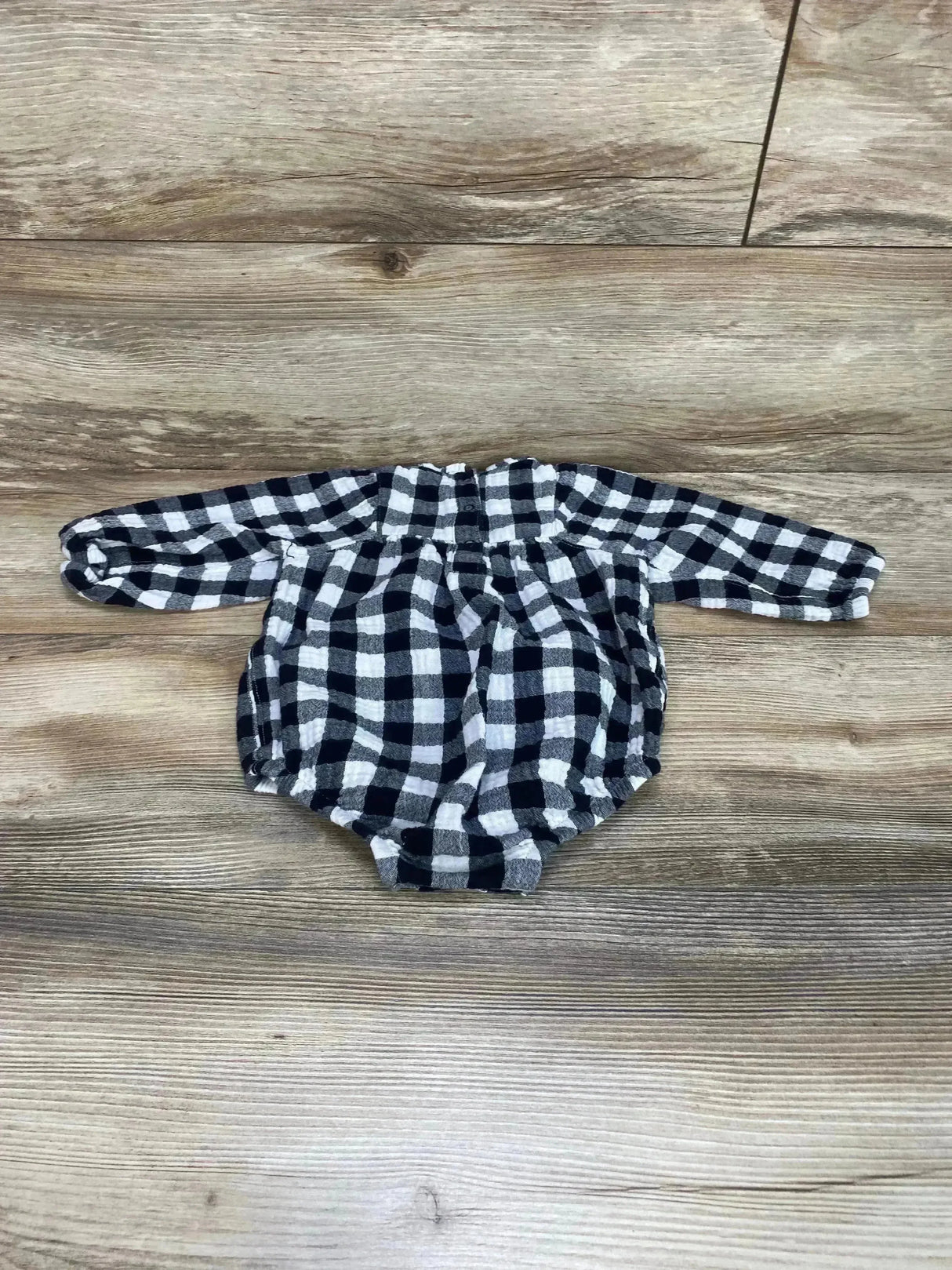 Flat lay of black-and-white buffalo check bubble romper showcasing long sleeves, gathered neckline, and elasticized leg openings on wood background