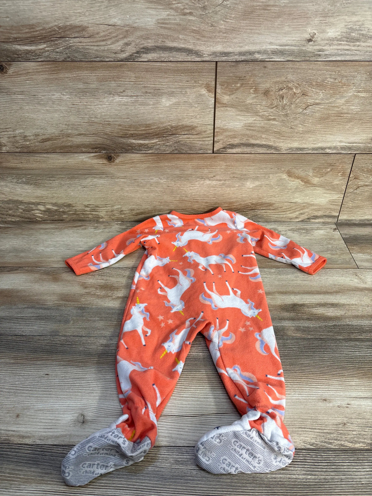 Front view of Child of Mine unicorn blanket sleeper in coral showcasing long sleeves, footed design, and unicorn print on a wood background