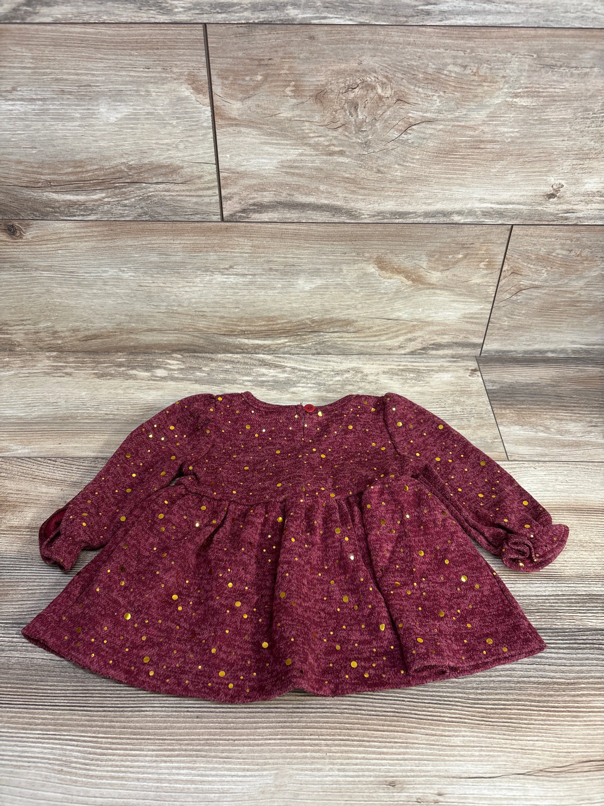Long sleeve maroon baby dress with gold polka dots on wood background