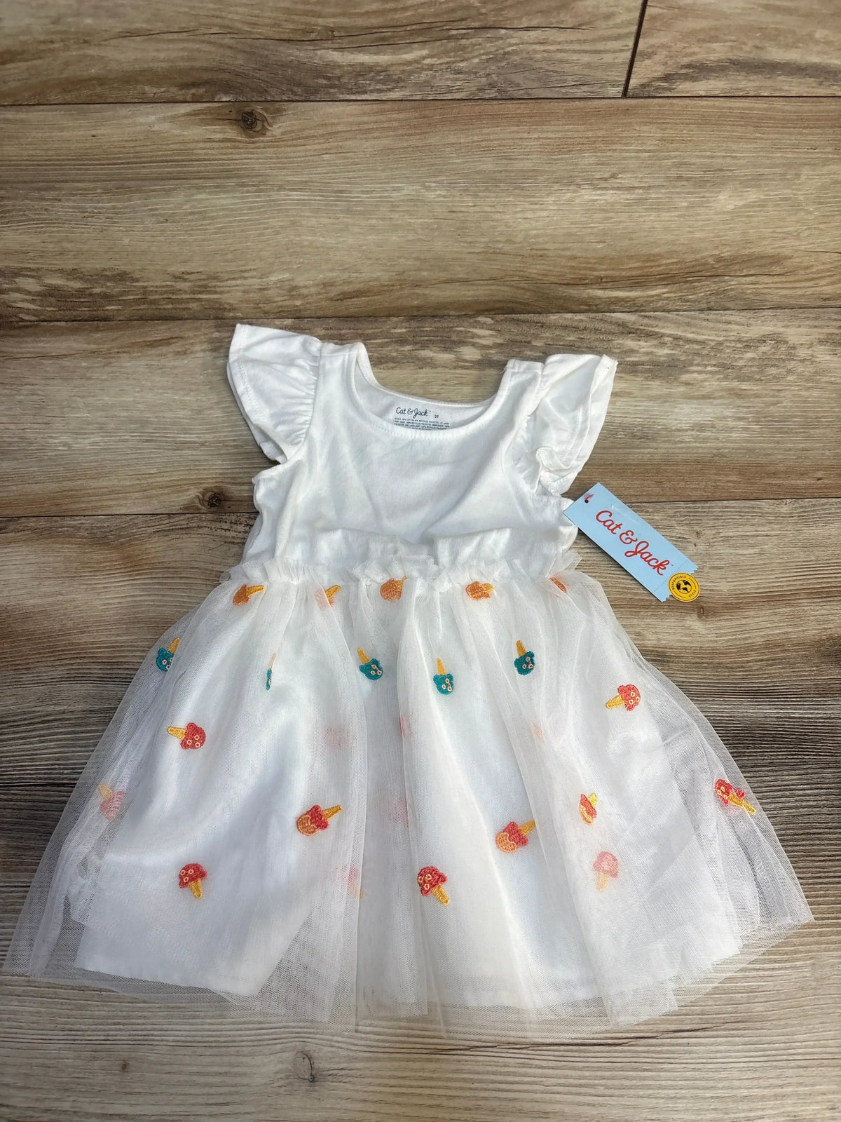 Flat lay of Cat & Jack white tulle tank dress showing ruffled sleeves and embroidered ice cream motifs on wood background