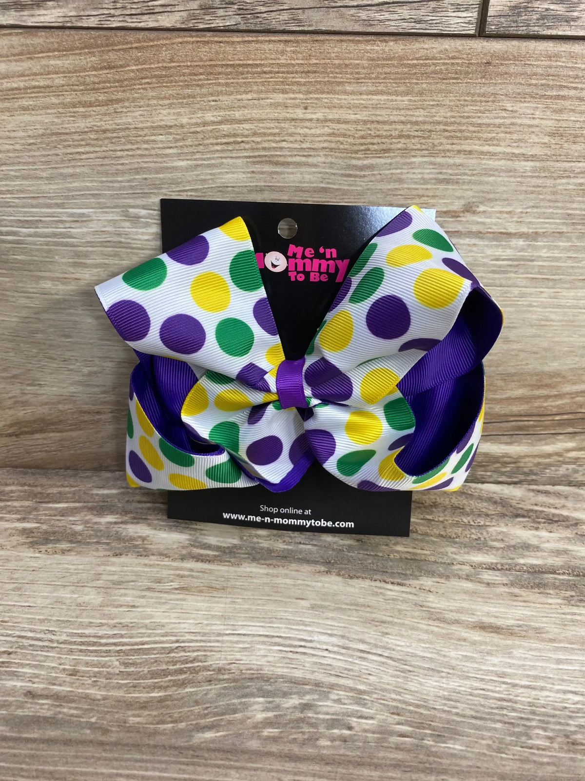 Front view of Mardi Gras polka-dot bow with white ribbon, green purple yellow dots, and purple backing on wood background