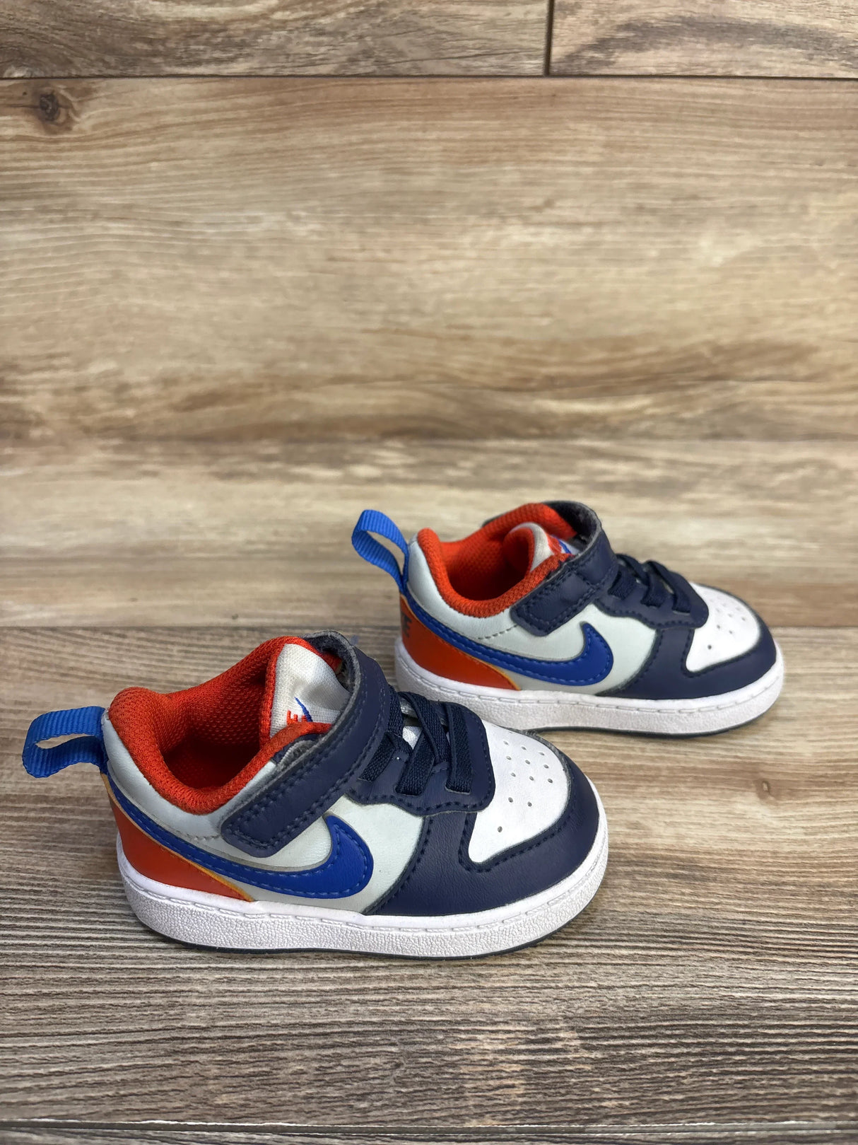 Pair of navy blue, white, and orange toddler sneakers with hook-and-loop straps on wood floor