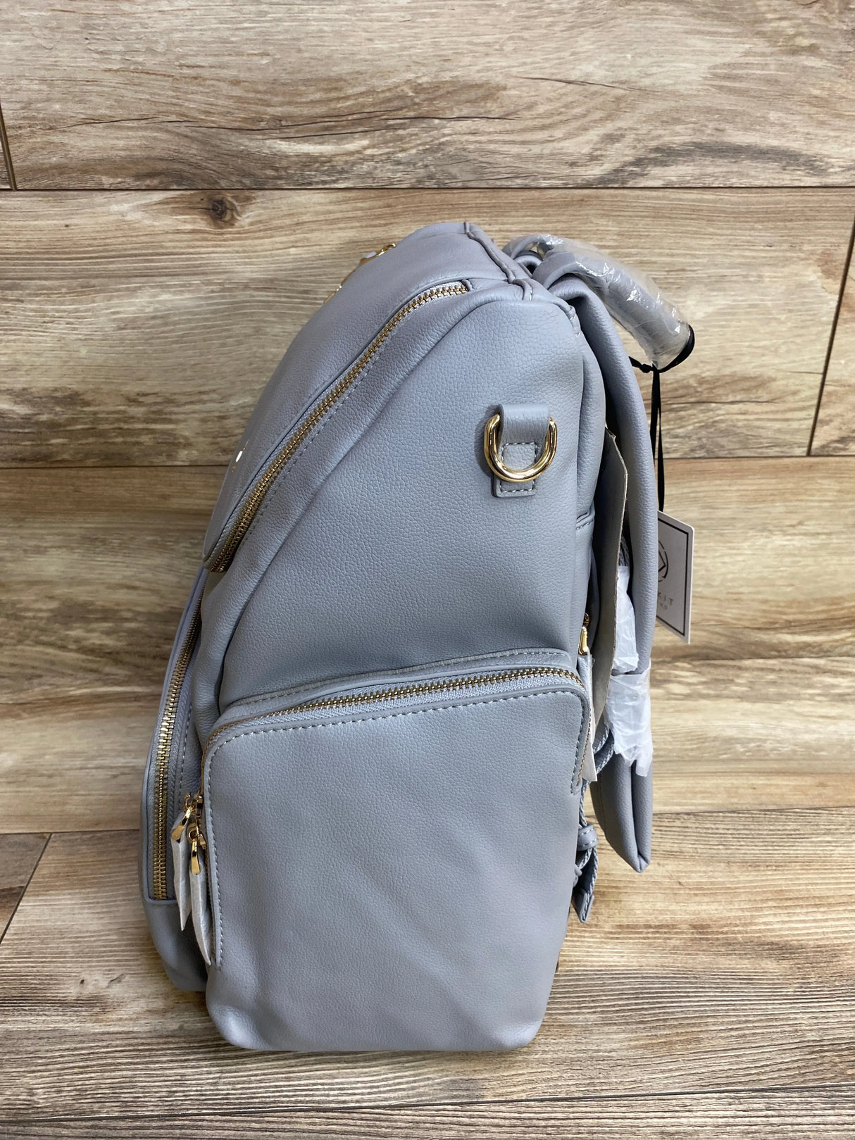 Gray diaper bag backpack with gold zippers and front pocket on wood background
