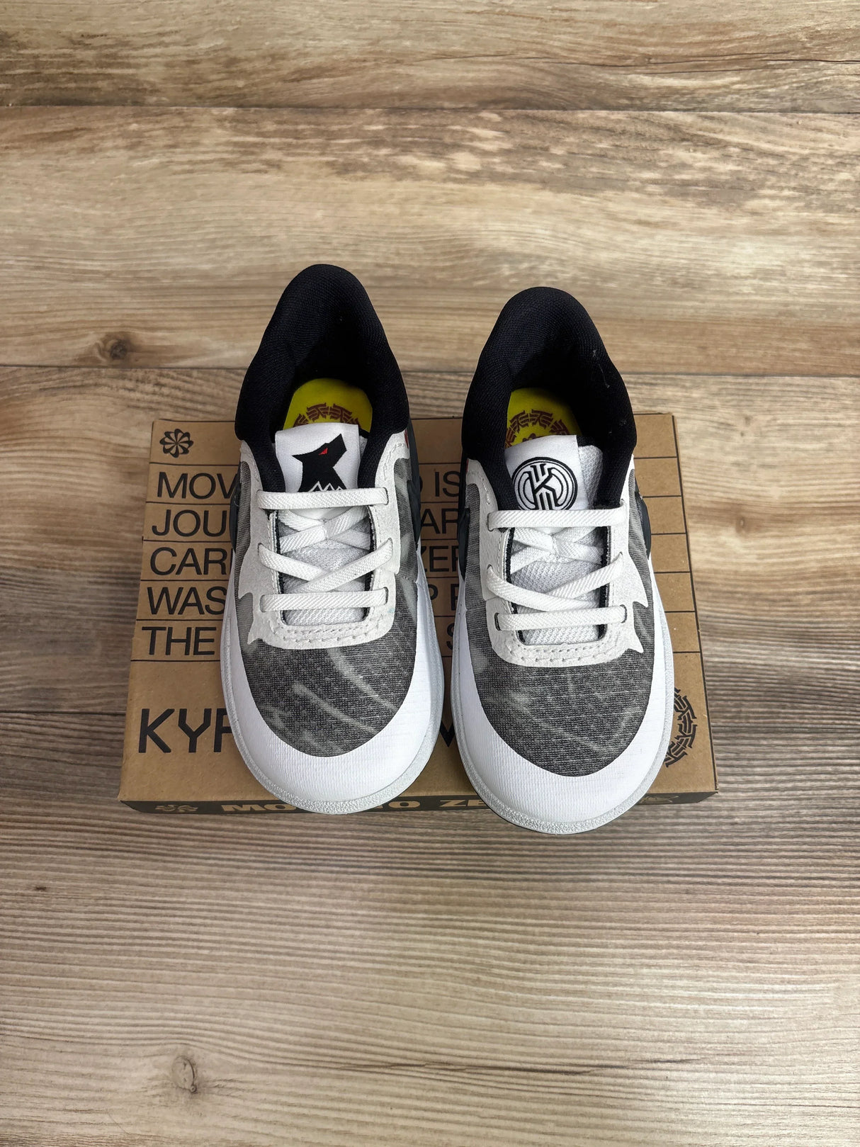 Top view of Nike Kyrie 8 toddler sneakers (size 9C) in white and gray with black collar and yellow insoles on a Kyrie shoebox on wood floor