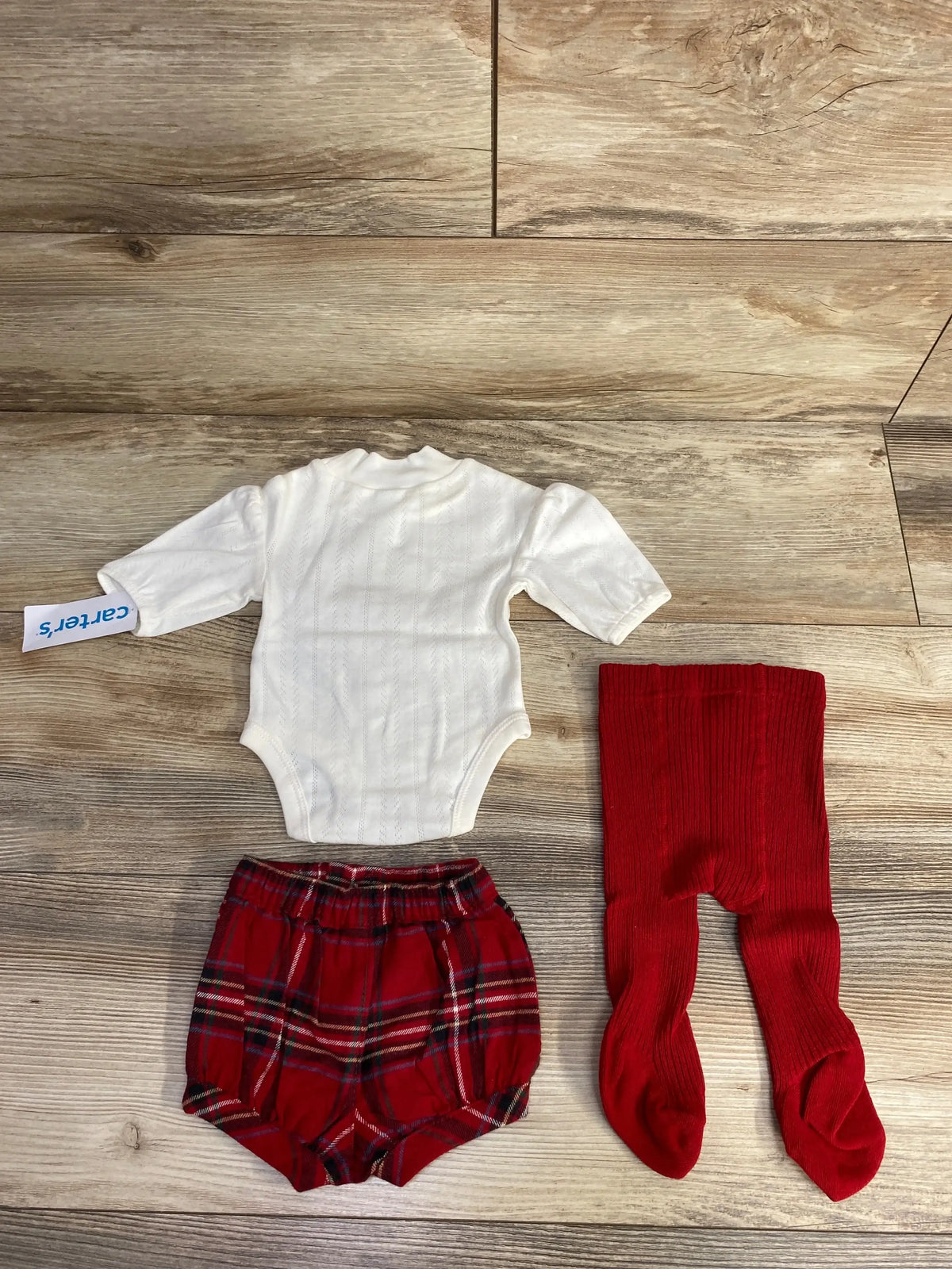 Carter's baby outfit with white bodysuit, red plaid shorts, and red ribbed tights on wood floor