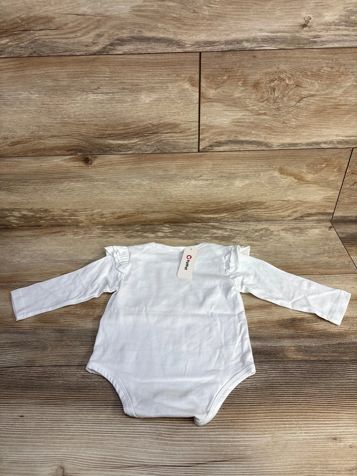 White long sleeve baby bodysuit with ruffles on shoulders on wood floor