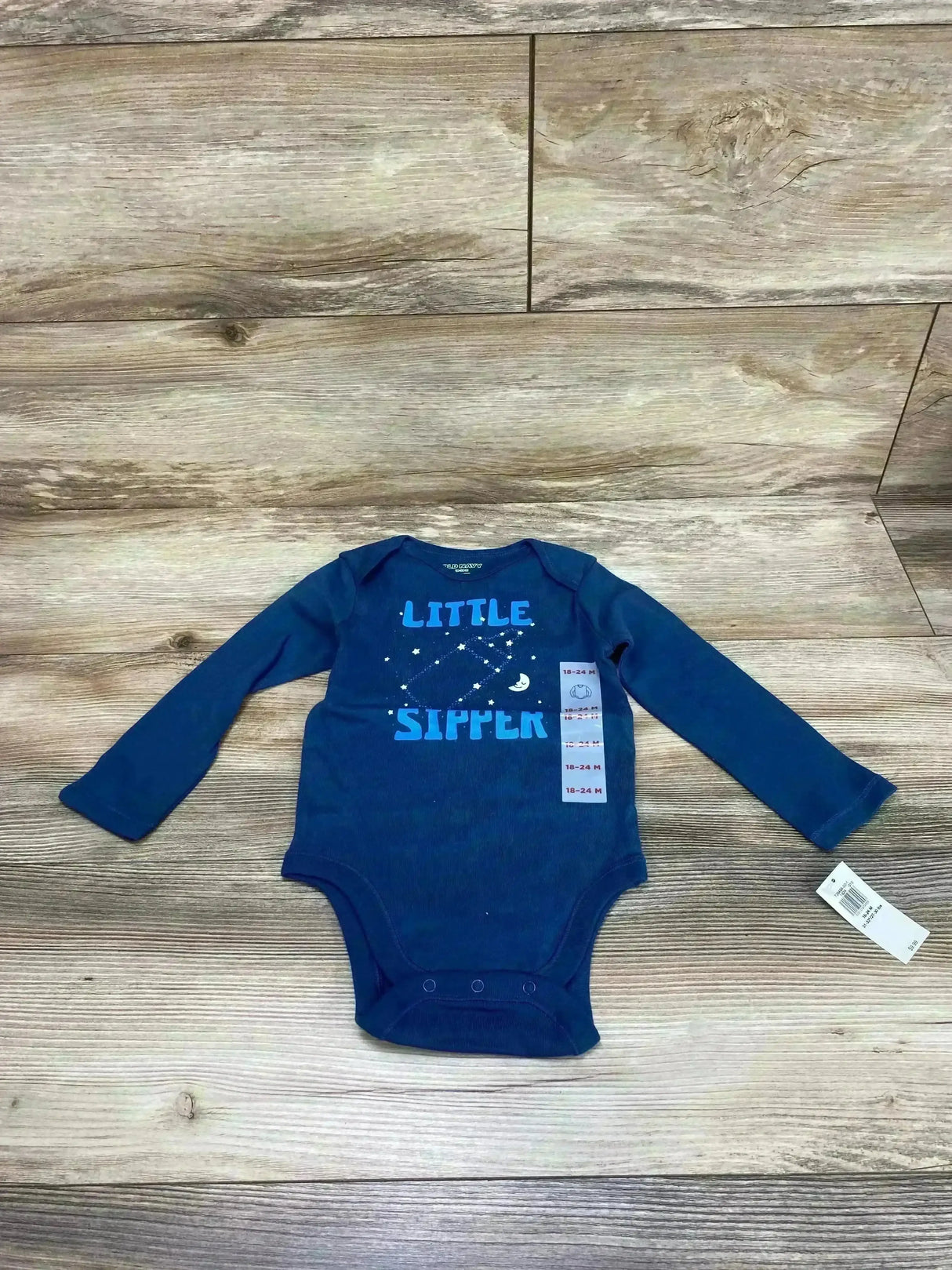 Front view of NEW Old Navy Blue Little Sipper Bodysuit sz 18-24m showcasing long-sleeve navy bodysuit with text graphic and attached hangtag on wood plank floor