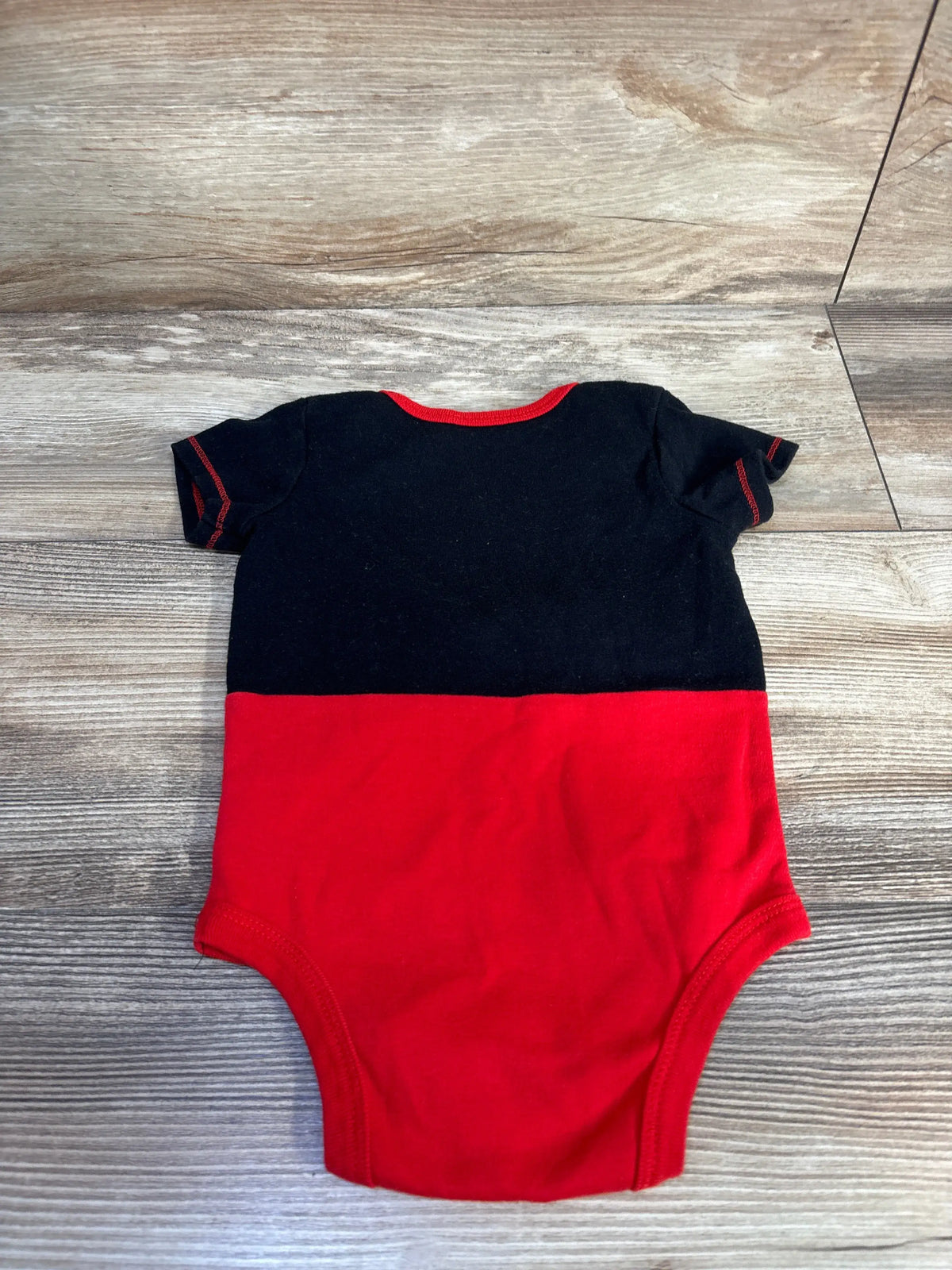Flat lay of Disney Baby Mickey Mouse bodysuit in size 12 months showcasing black-and-red color blocking on a wood-look floor