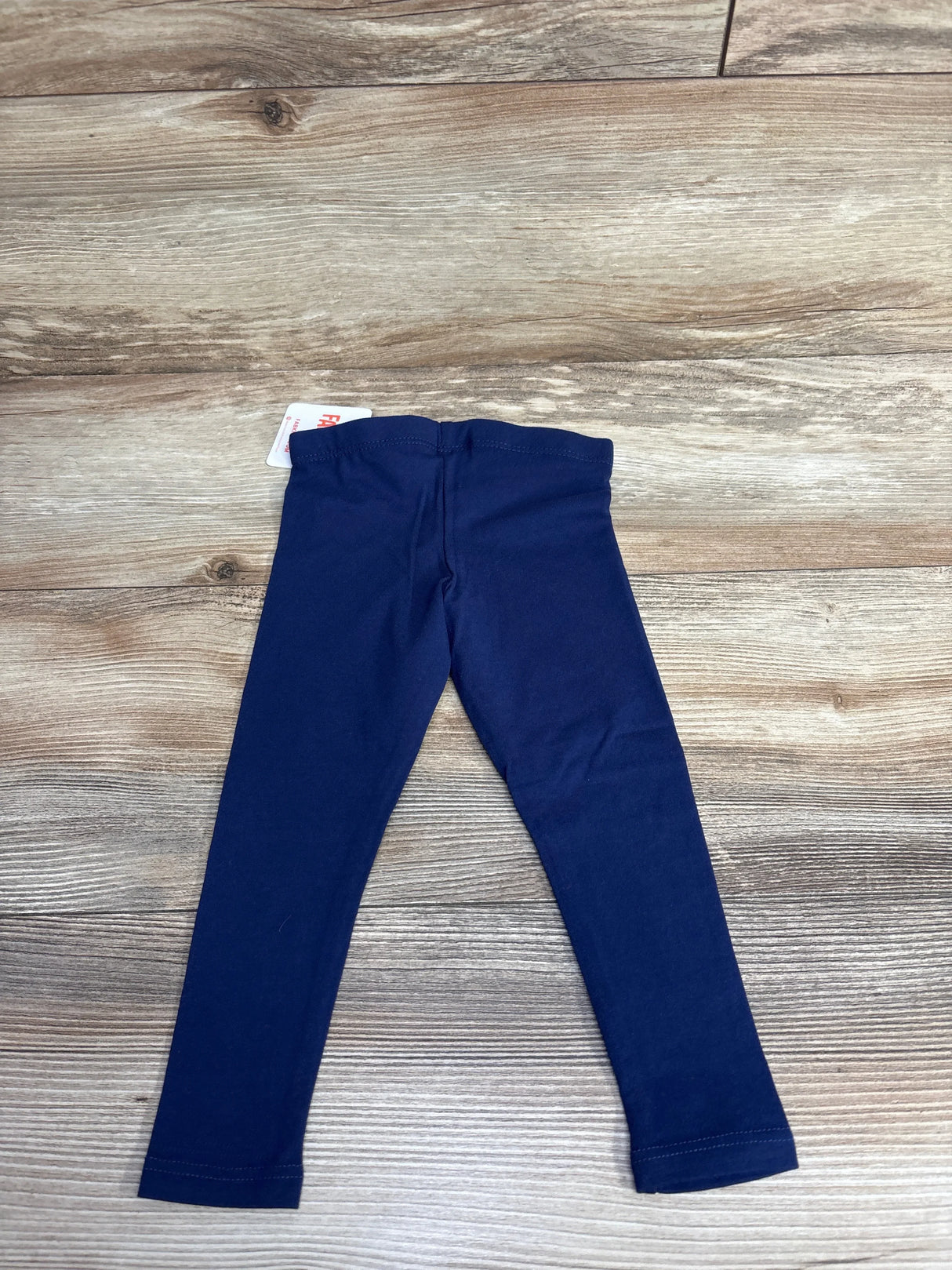 Navy blue children's leggings laid flat on wood floor background, kids clothing item