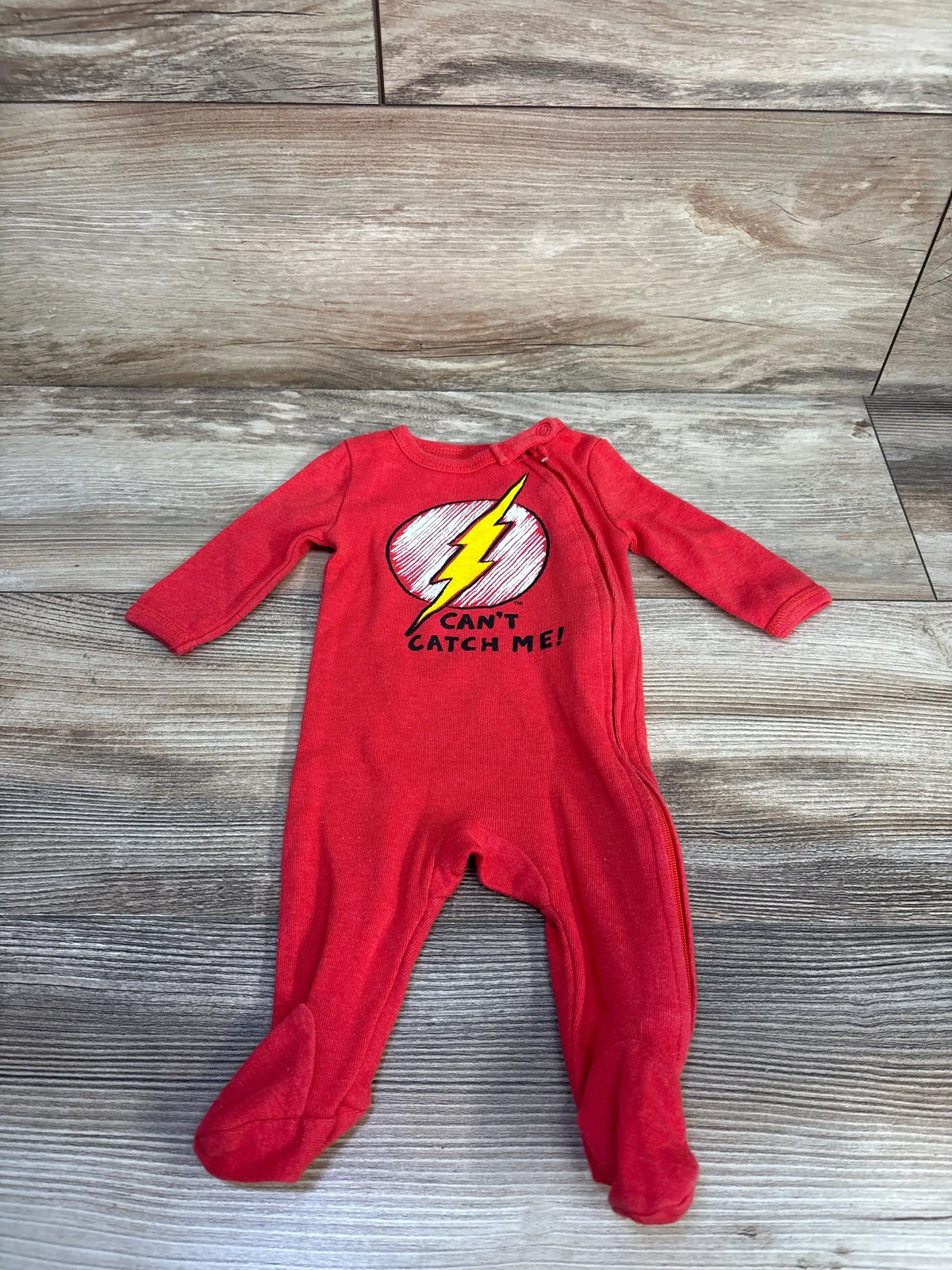 Front view of a red Flash newborn sleeper showcasing footed legs and a Can’t Catch Me lightning bolt graphic on a wood-look floor