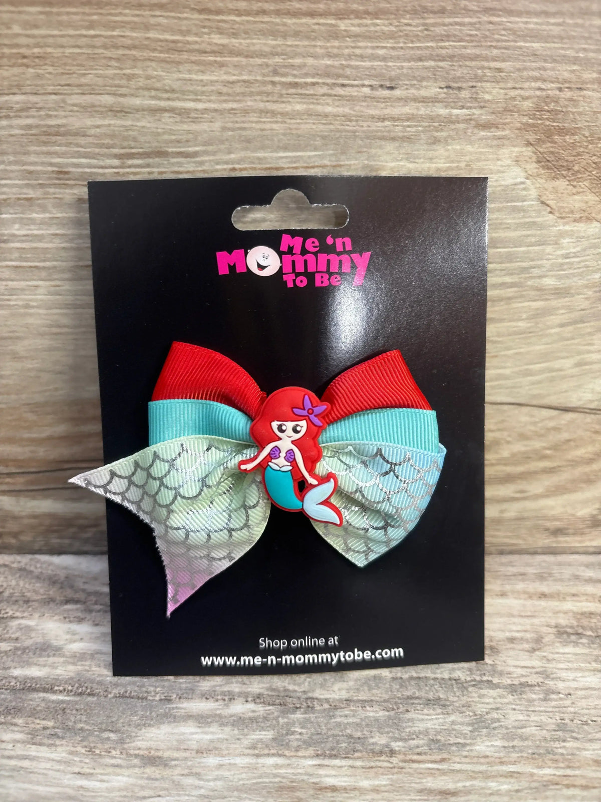Front view of mermaid applique hair bow with red and teal layered ribbons and scale-pattern tails on black display card