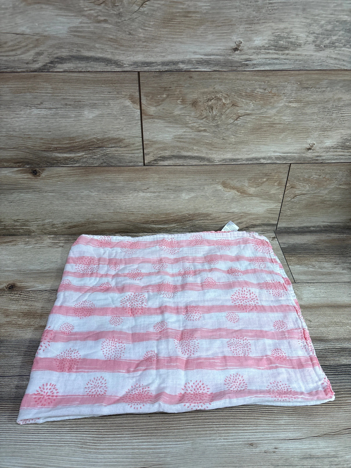 Front view of GLLQUEN pink and white striped swaddle blanket with dotted floral pattern on a wood surface
