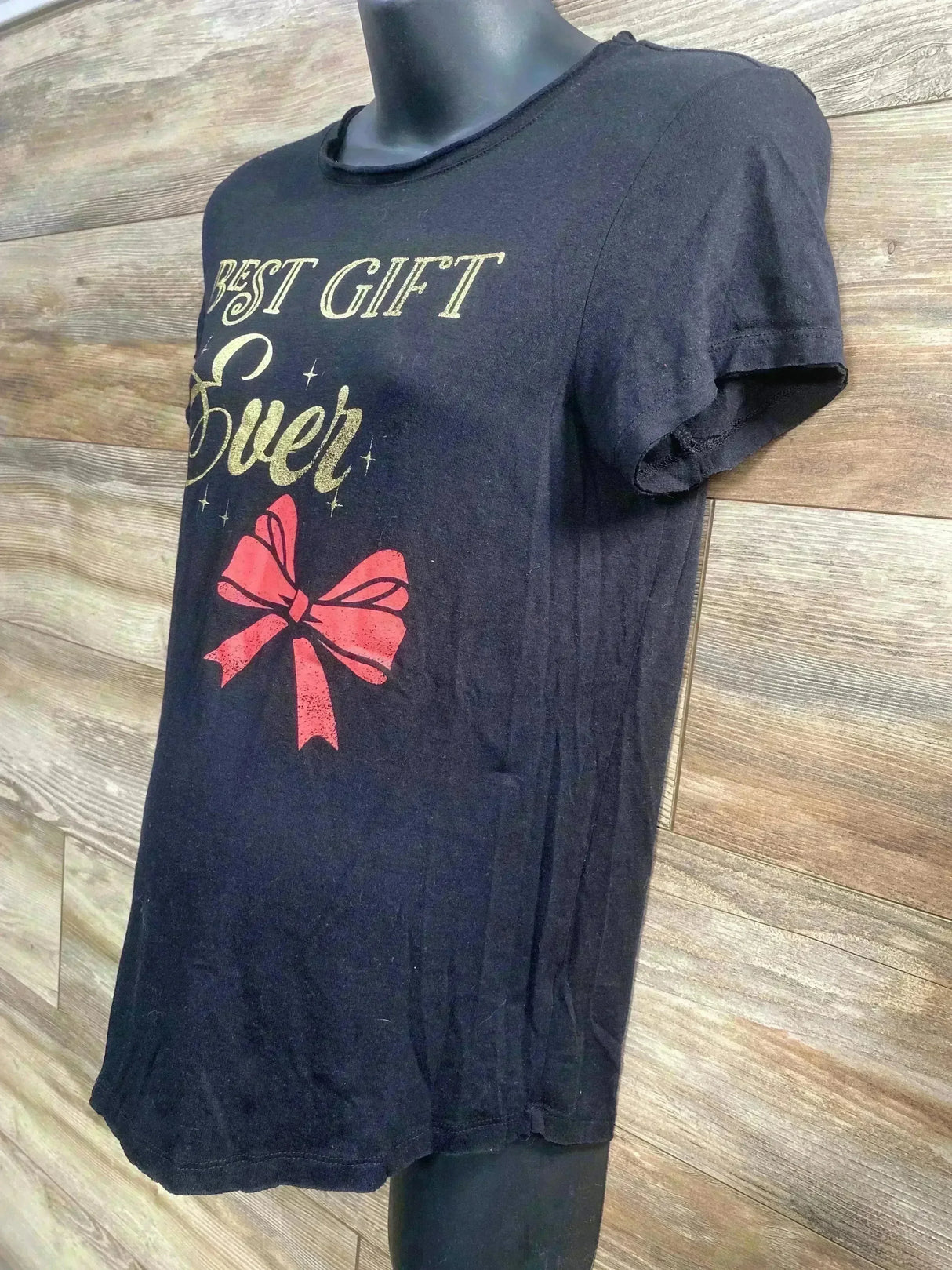 Side front view of Isabel maternity black tee showing gold Best Gift Ever text and red bow on wood background