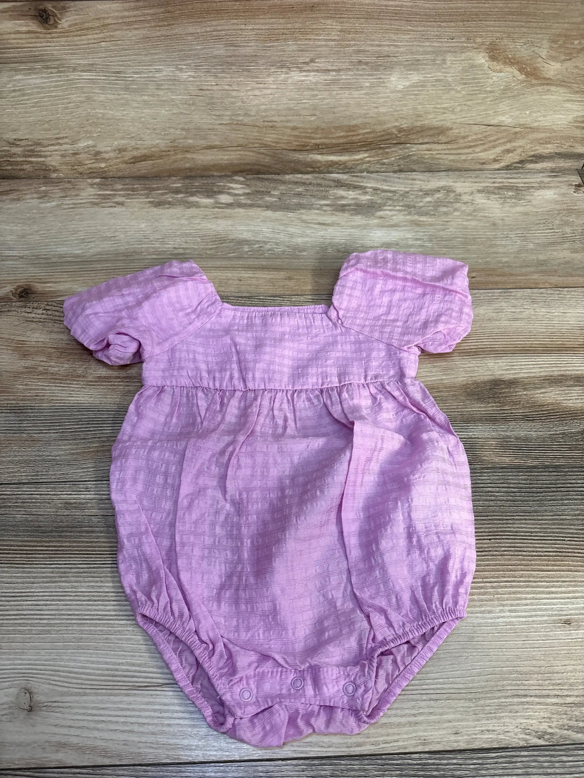 Top view of Cat & Jack purple bubble romper with puff sleeves, gathered waist and crotch snaps on wood background