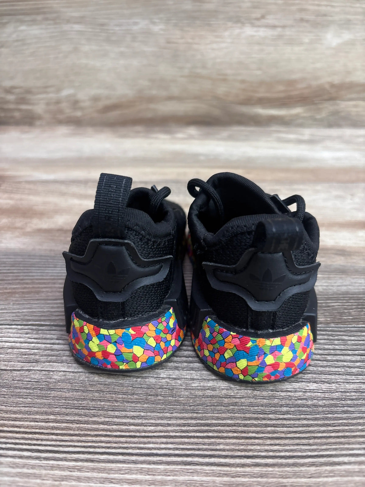 Rear view of black Adidas NMD_R1 El Mosaic sneakers with colorful patterned soles.