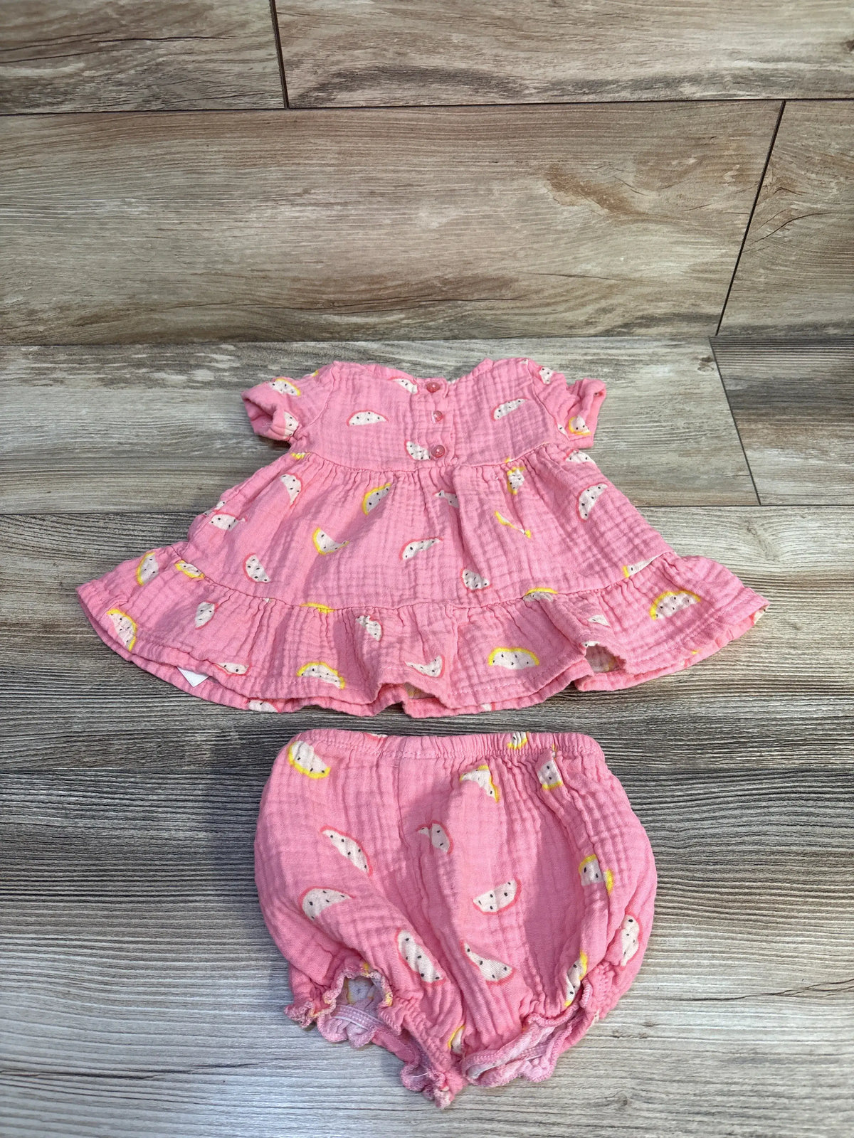 Flat lay of pink gauze 2-piece dress and bloomers showing ruffle hem, button-back, and koala print on wood background