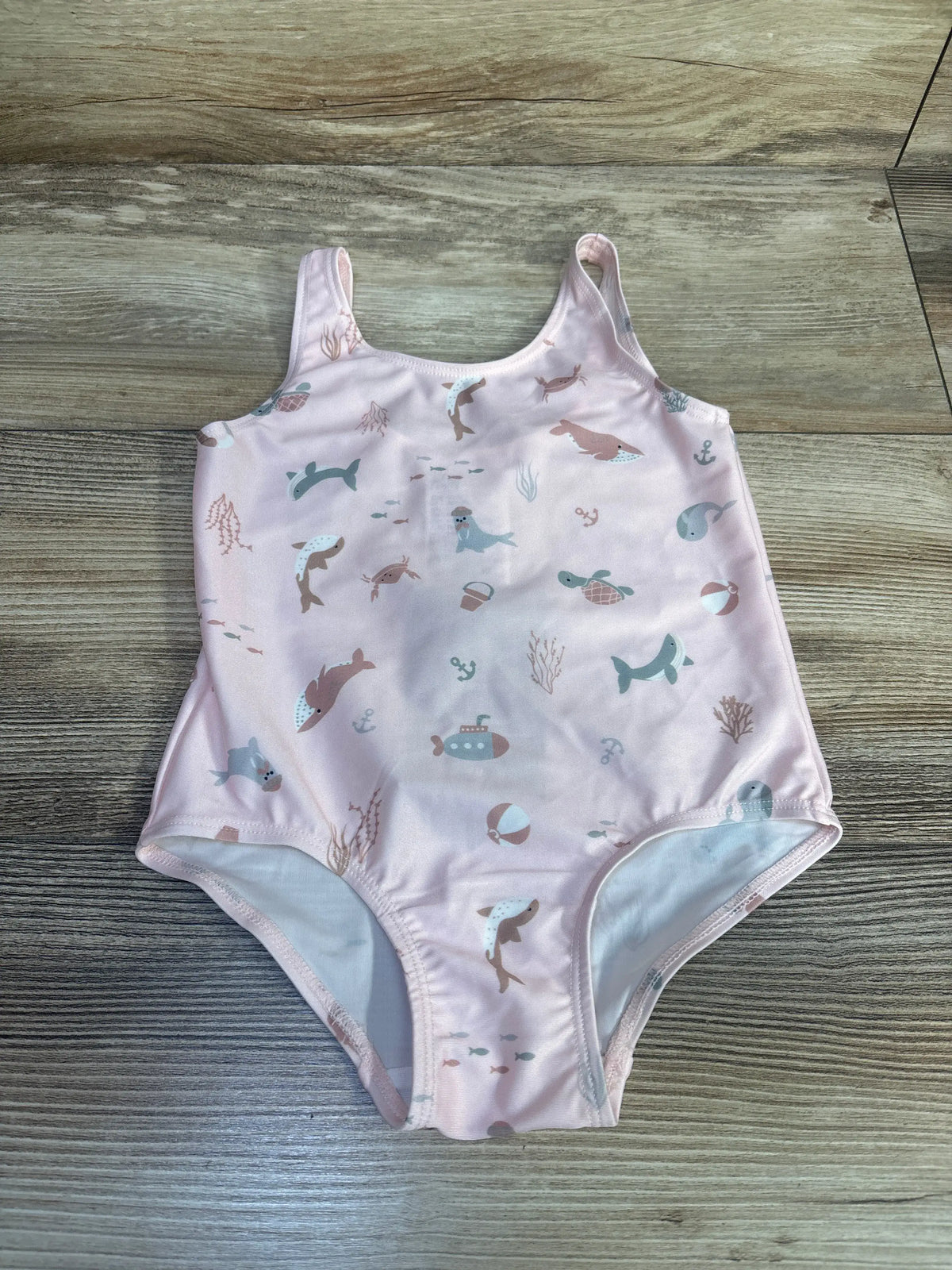 Front view of a pink H&M one-piece swimsuit showcasing an aquatic animal pattern with a wood-grain background