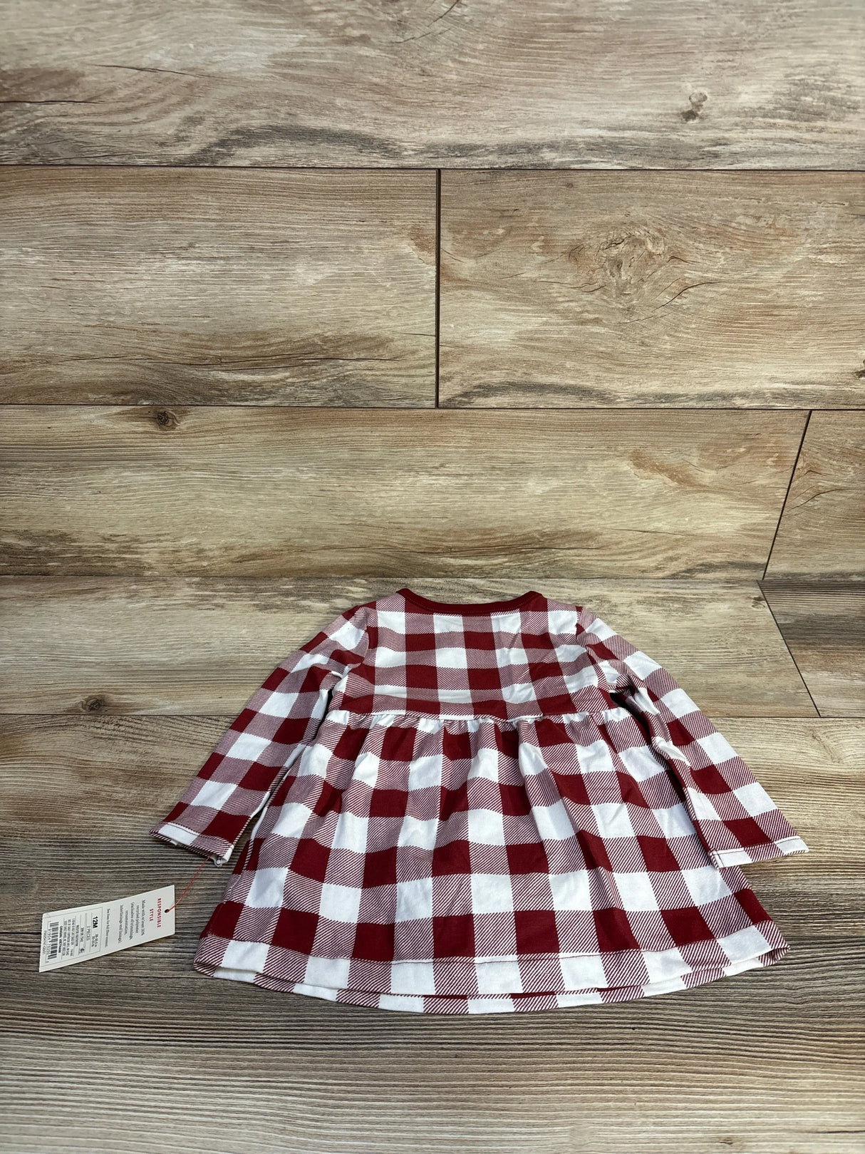 Red and white plaid long sleeve baby dress with tag on wood floor