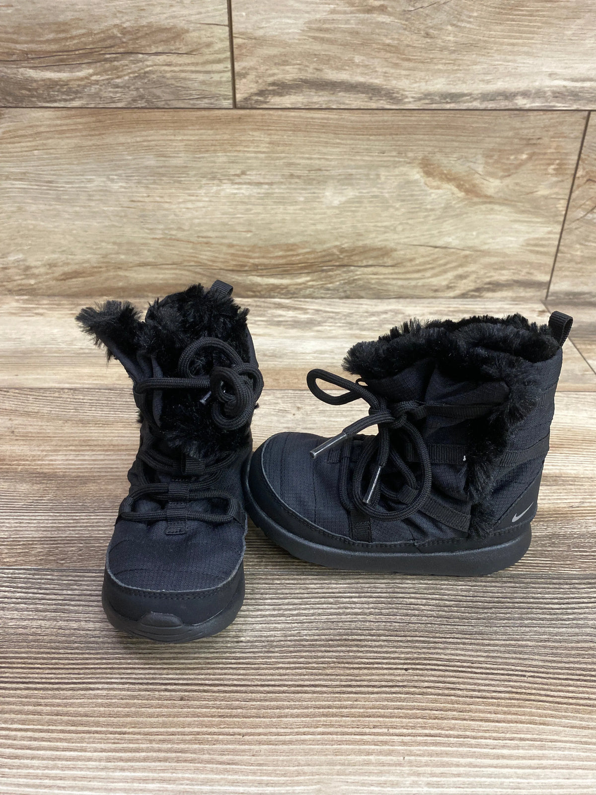 Front and side views of black Nike Roshe One High TDV winter boots showcasing fuzzy collars and laces on a wood-look floor