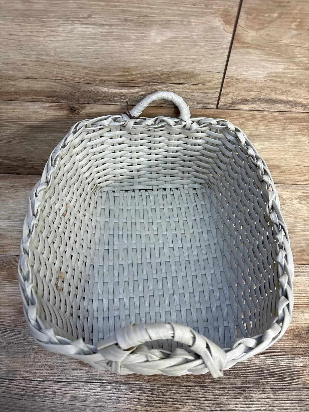 Light gray woven wicker basket with handles, ideal for nursery storage or baby gear organization on wood floor