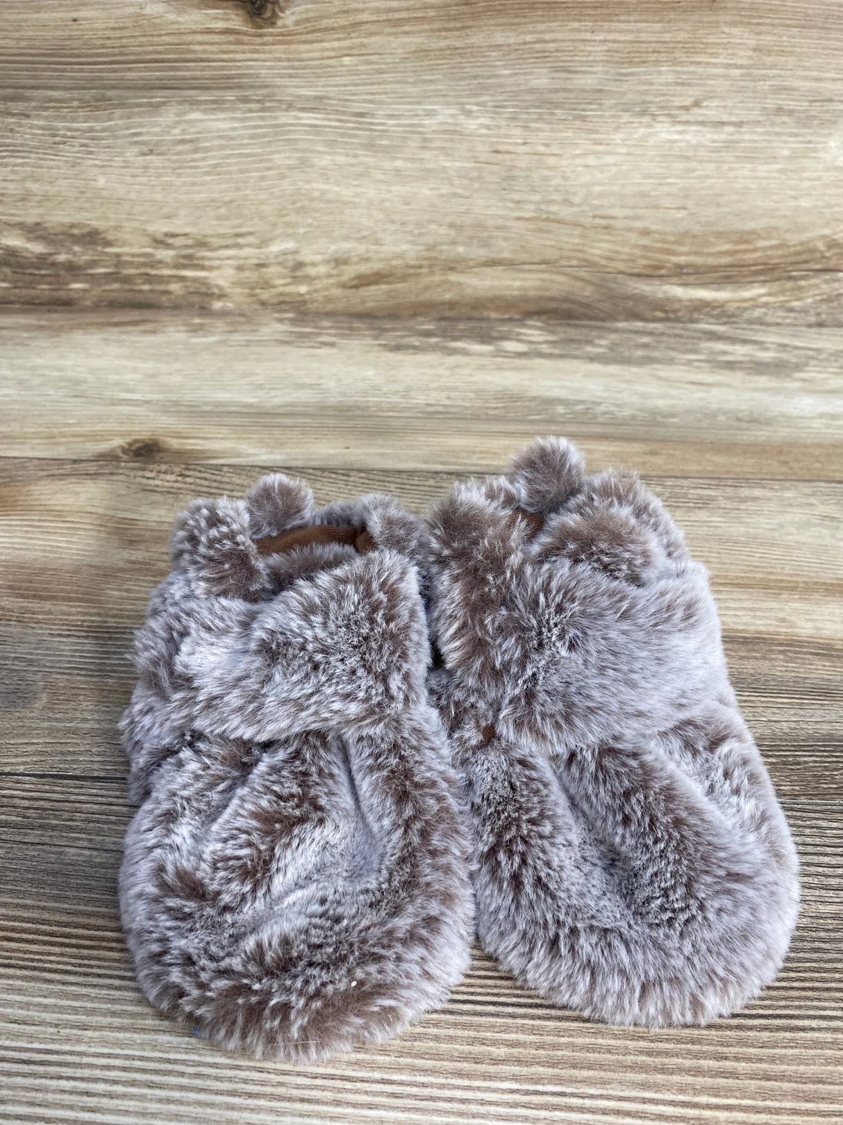 Plush fuzzy slippers in light brown on wooden floor, cozy home footwear