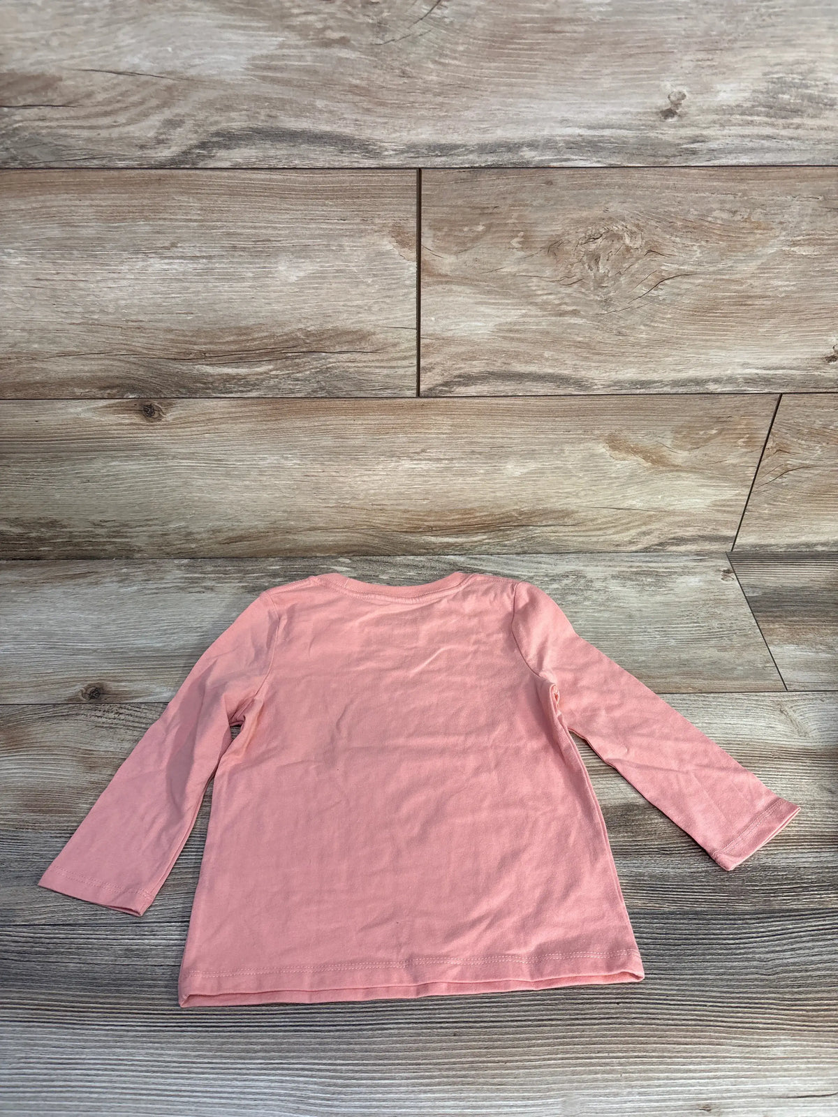 Front view of Cat & Jack pink long sleeve shirt in size 2T showcasing relaxed fit with wood-patterned background