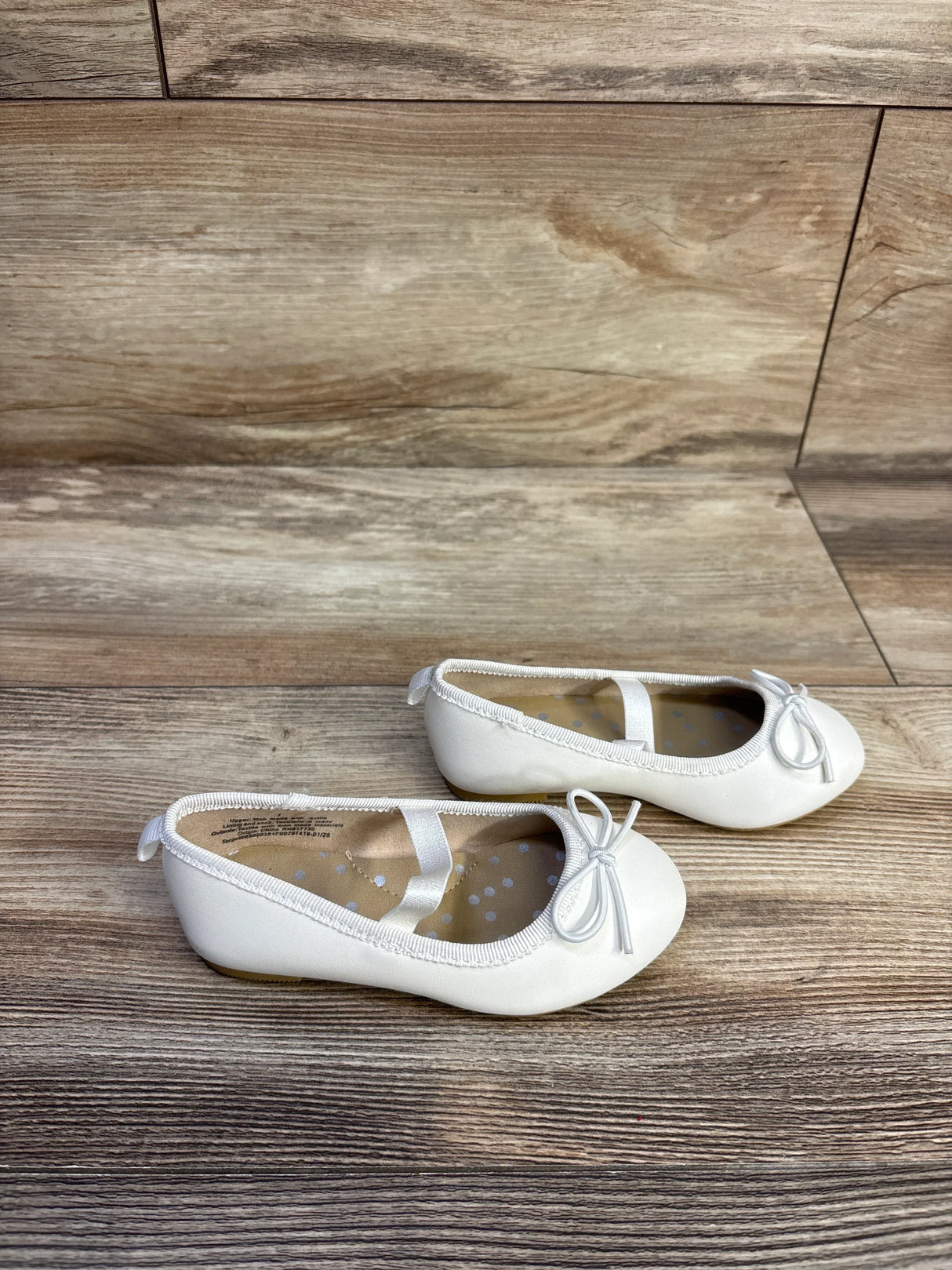 Side view of Cat and Jack Nora slip-on white toddler ballet flats size 7C showcasing elastic strap and bow detail on wood floor background