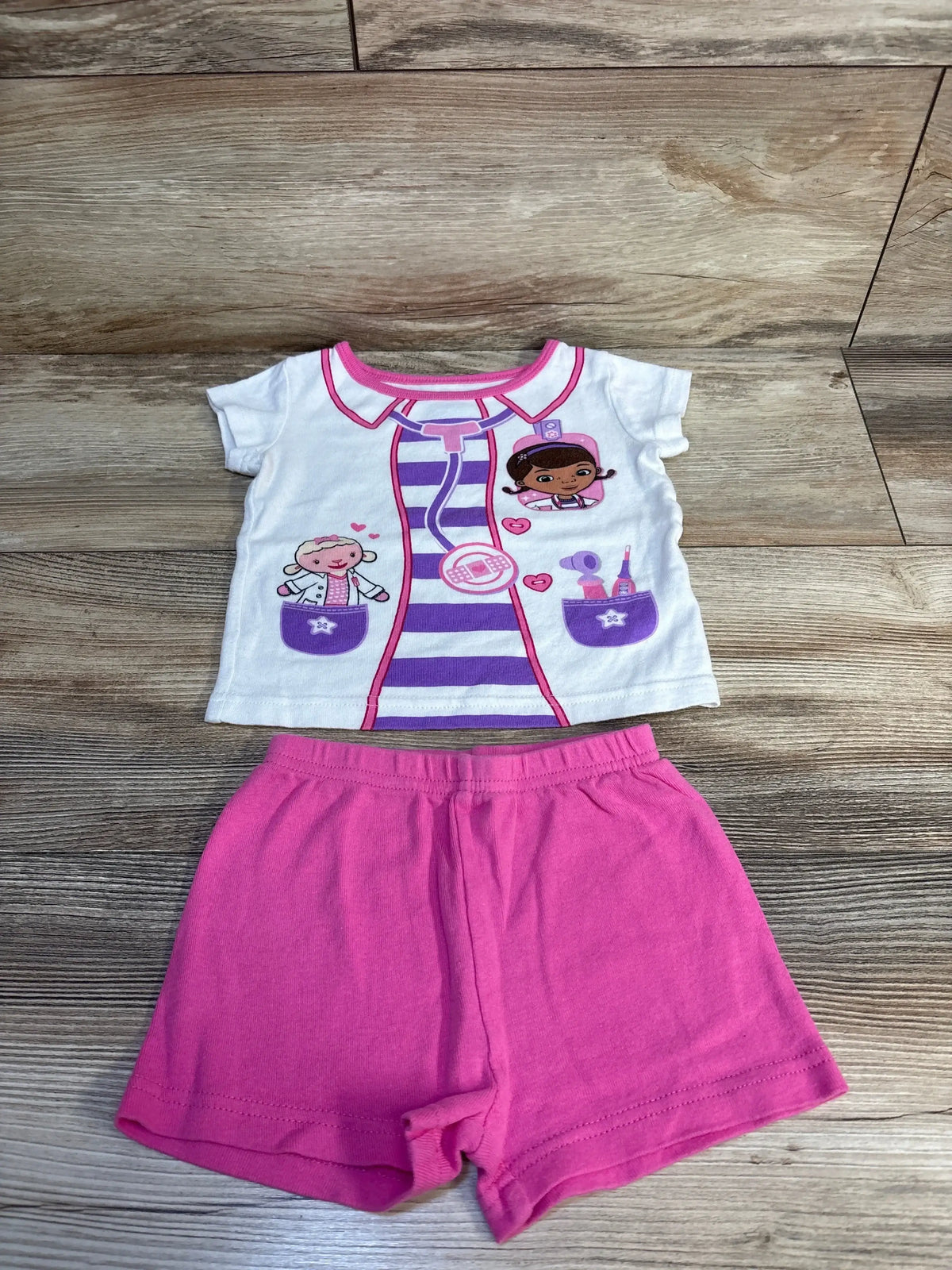 Toddler girl's Doc McStuffins character t-shirt and pink shorts set on wood floor