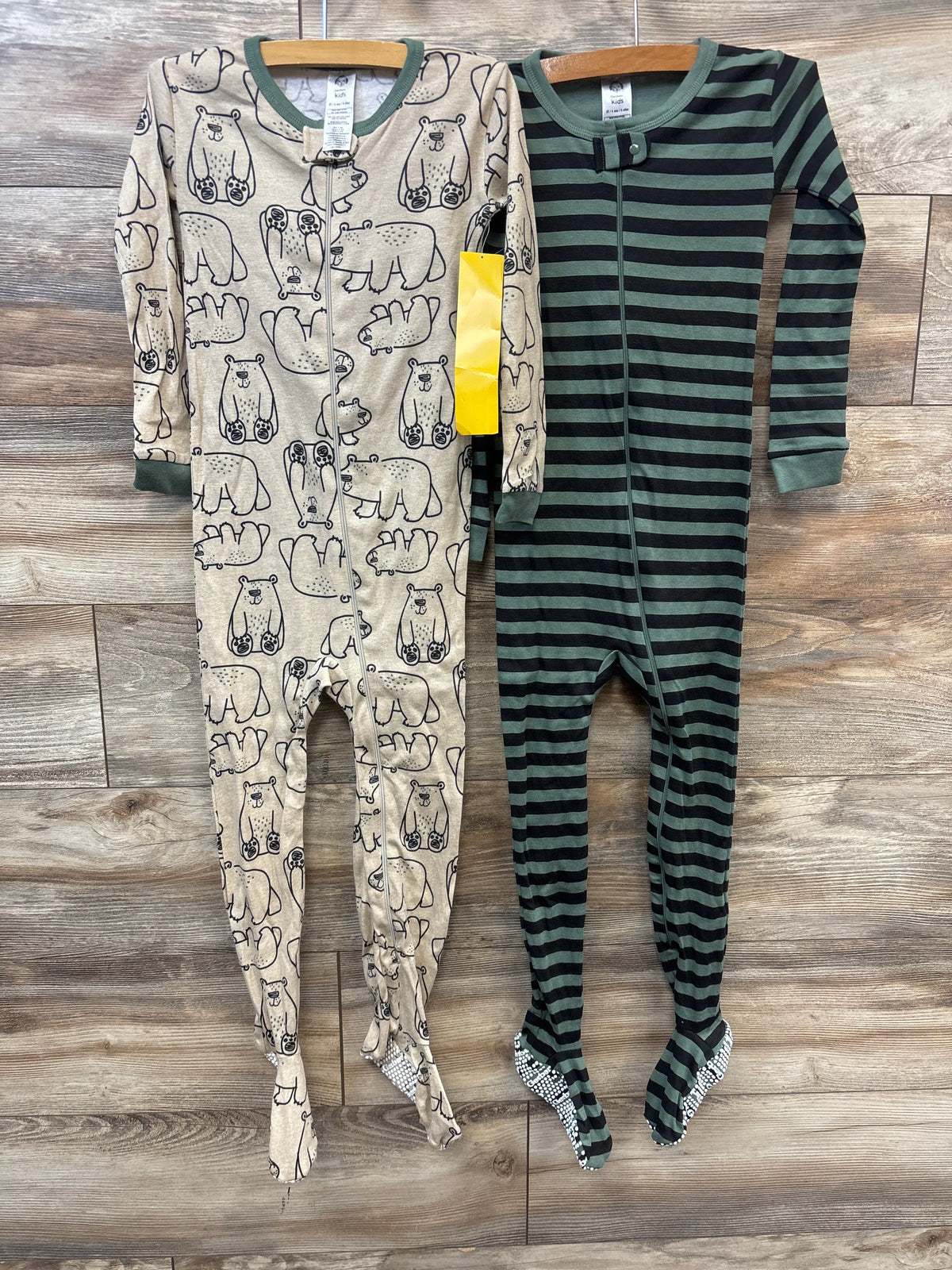 Front view of two Gerber Sleep N Play sleepers with animal prints, green stripes, zippers, and foot coverings on wood floor