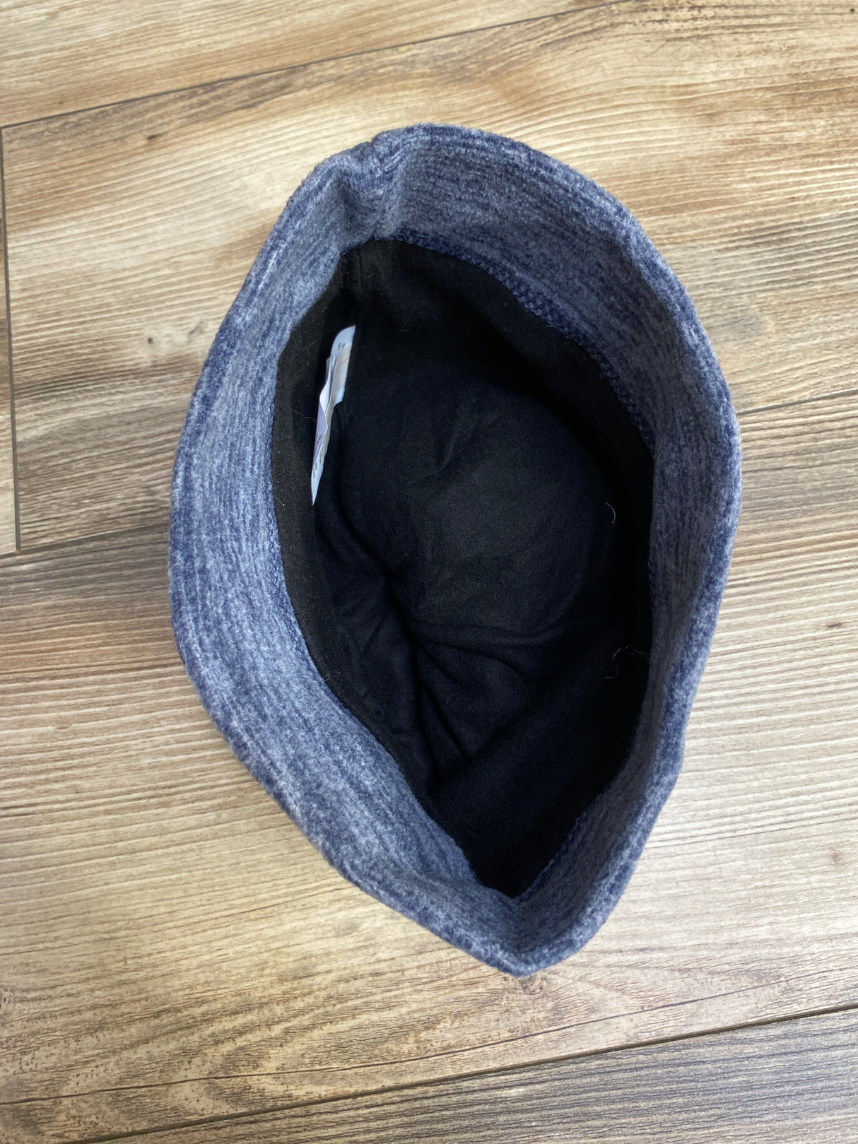 Top view of a blue knit wool hat with black inner lining on wooden floor