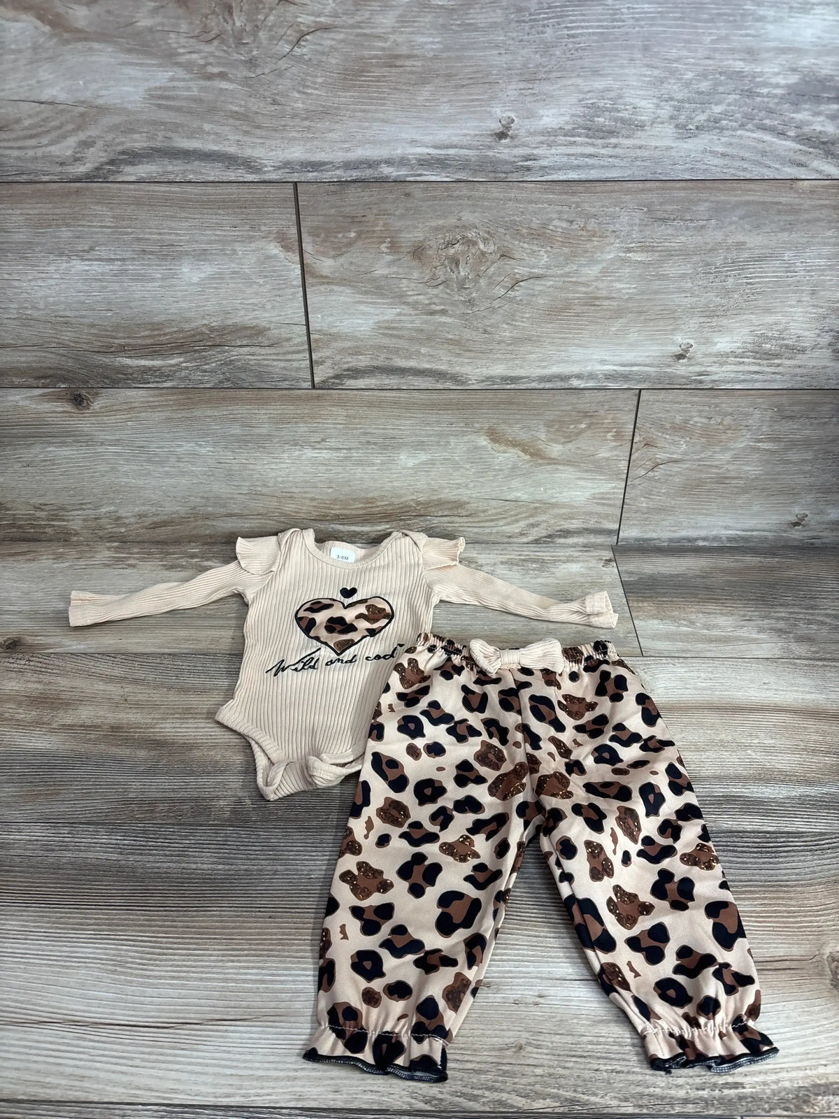 Top down view of tan ribbed baby bodysuit with ruffle shoulders and matching leopard-print pants on light wood surface