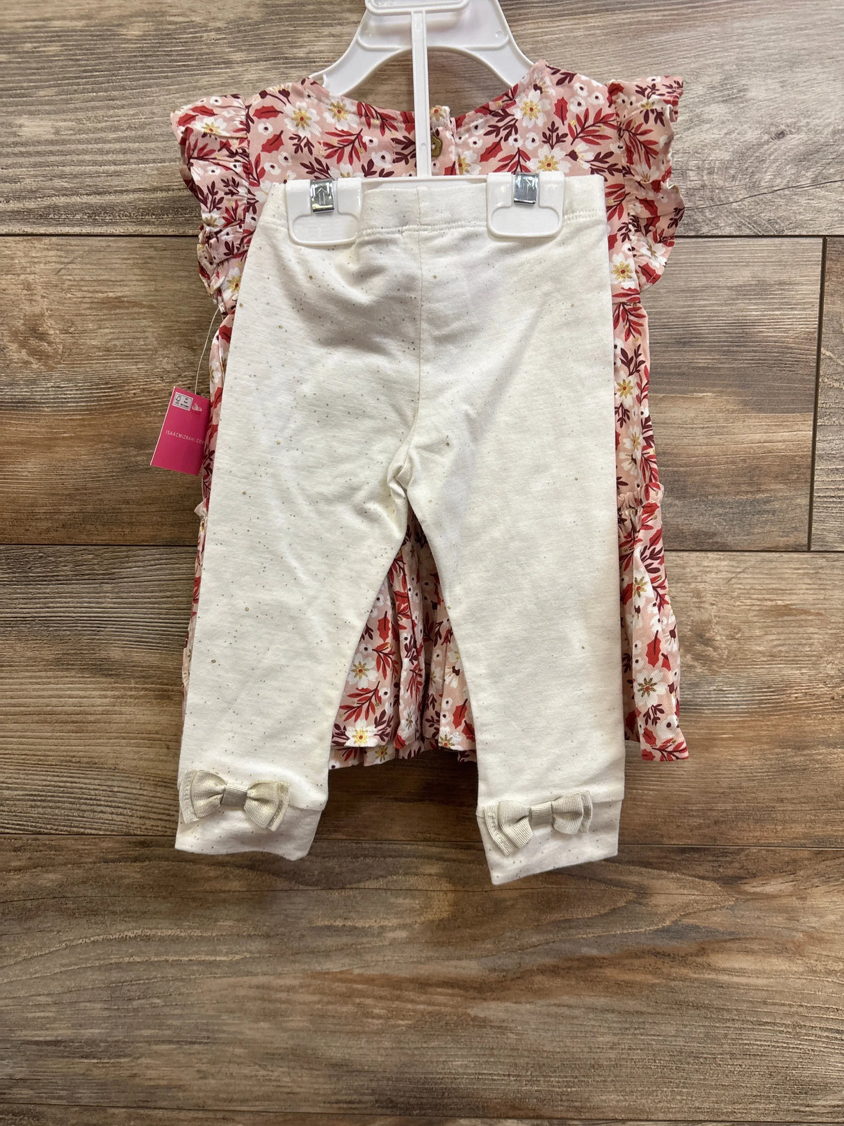 Front view of pink smocked floral dress and cream leggings showing ruffle sleeves and bow cuffs on wood background