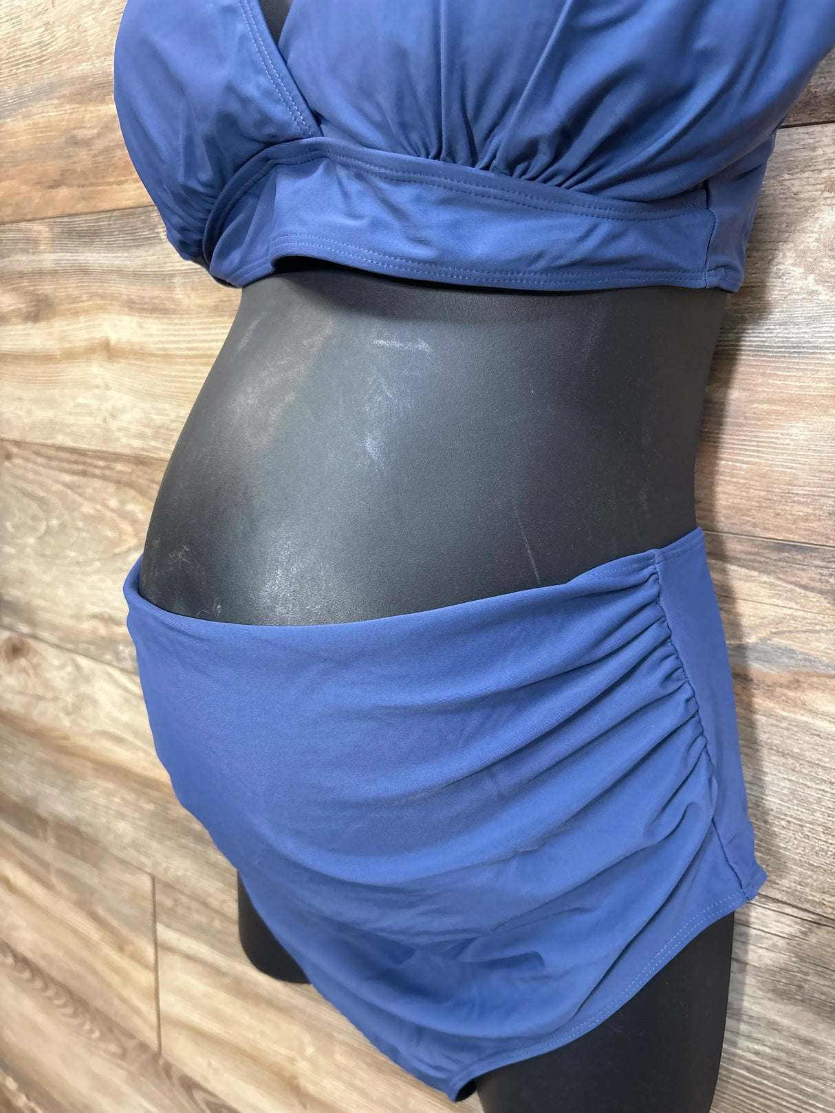 Side view of navy maternity two-piece swimsuit showing ruched high-waist bottom and gathered top on wood background