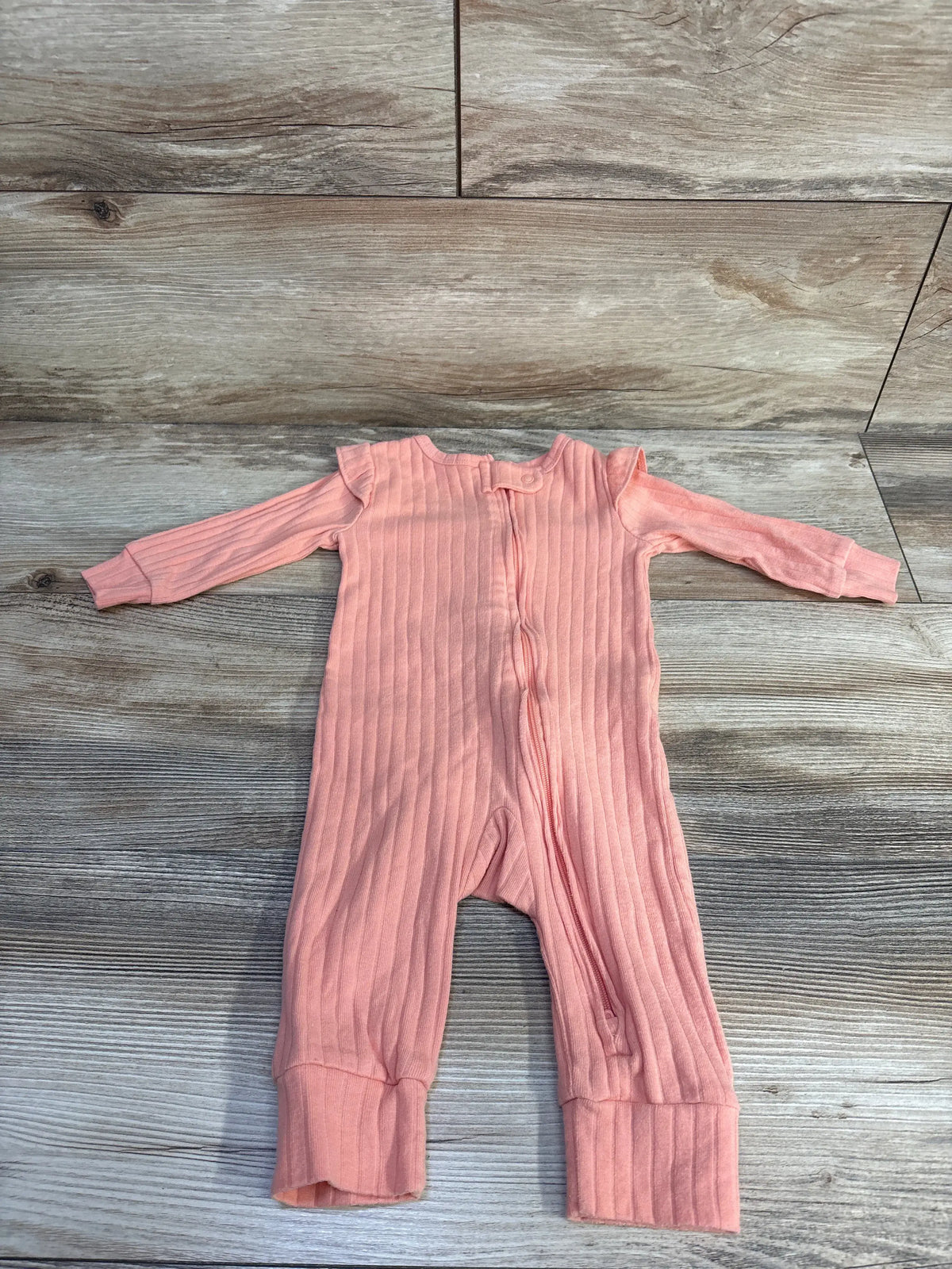 Front view of Carter’s coral ribbed footless coverall showcasing ruffle sleeves and two way zipper on a wood background