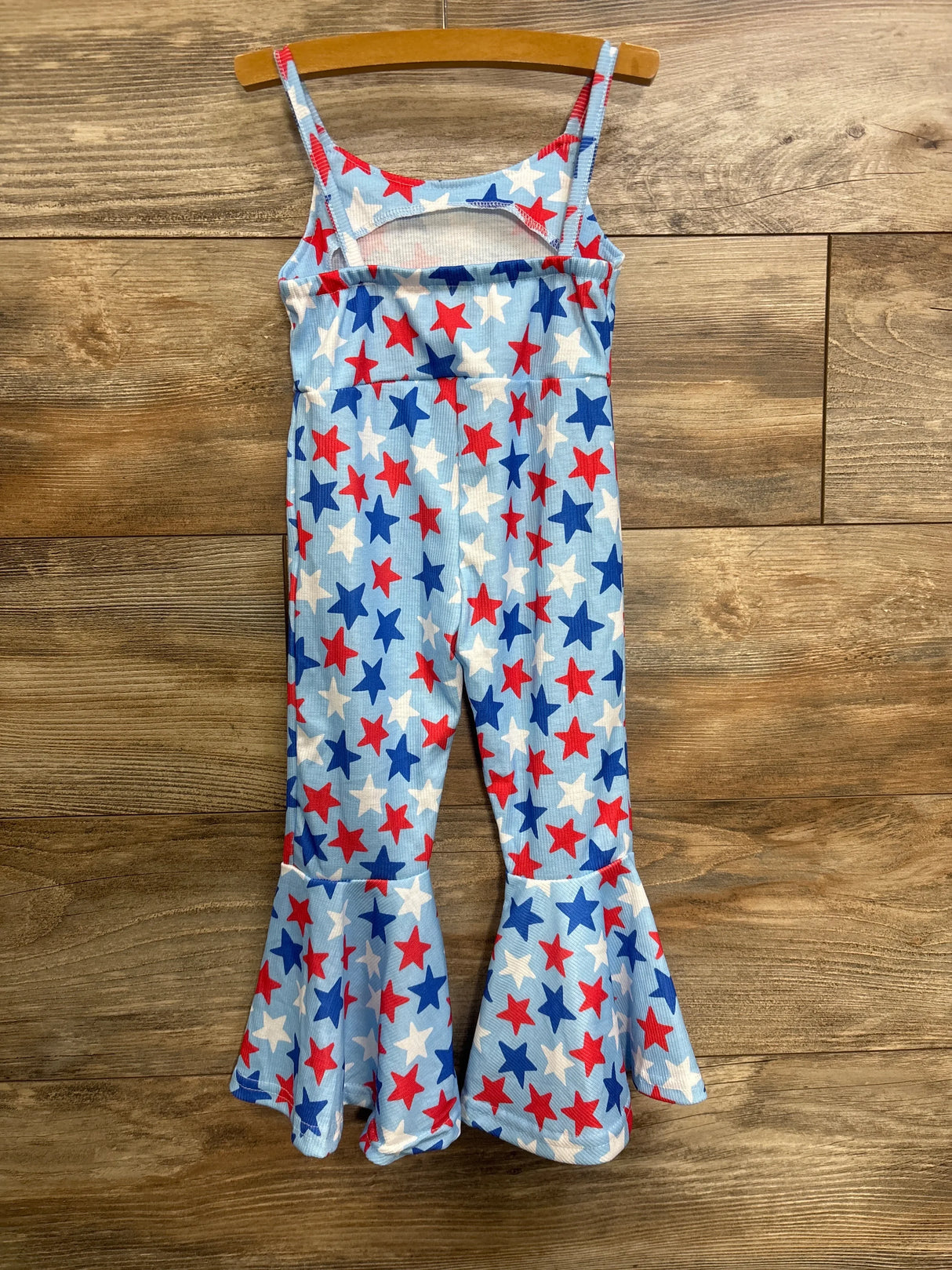 Front view of blue bell-bottom jumpsuit with red, white and blue star print and ruffled flared legs on wooden background