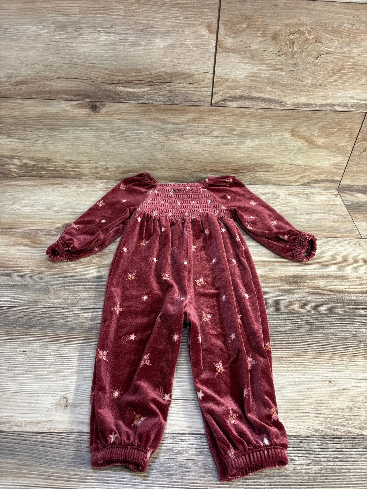 Flat-lay of red velvet smocked baby coverall showing smocked chest, long puff sleeves, elastic cuffs, and star print on wood background