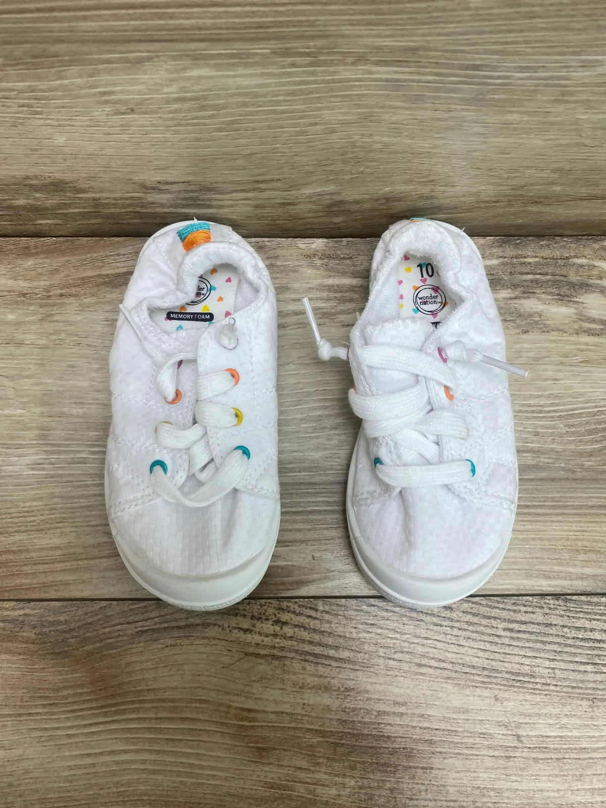 Top-down view of white Wonder Nation girls' sneakers with textured upper and multicolor eyelets on wood floor