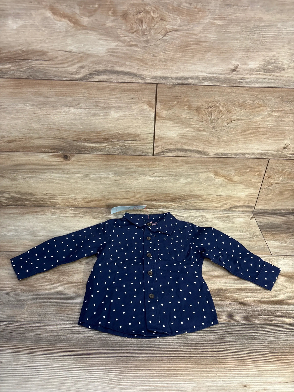 Front view of Cat & Jack navy polka dot button-up shirt showcasing long sleeves and front buttons on a wood-look floor