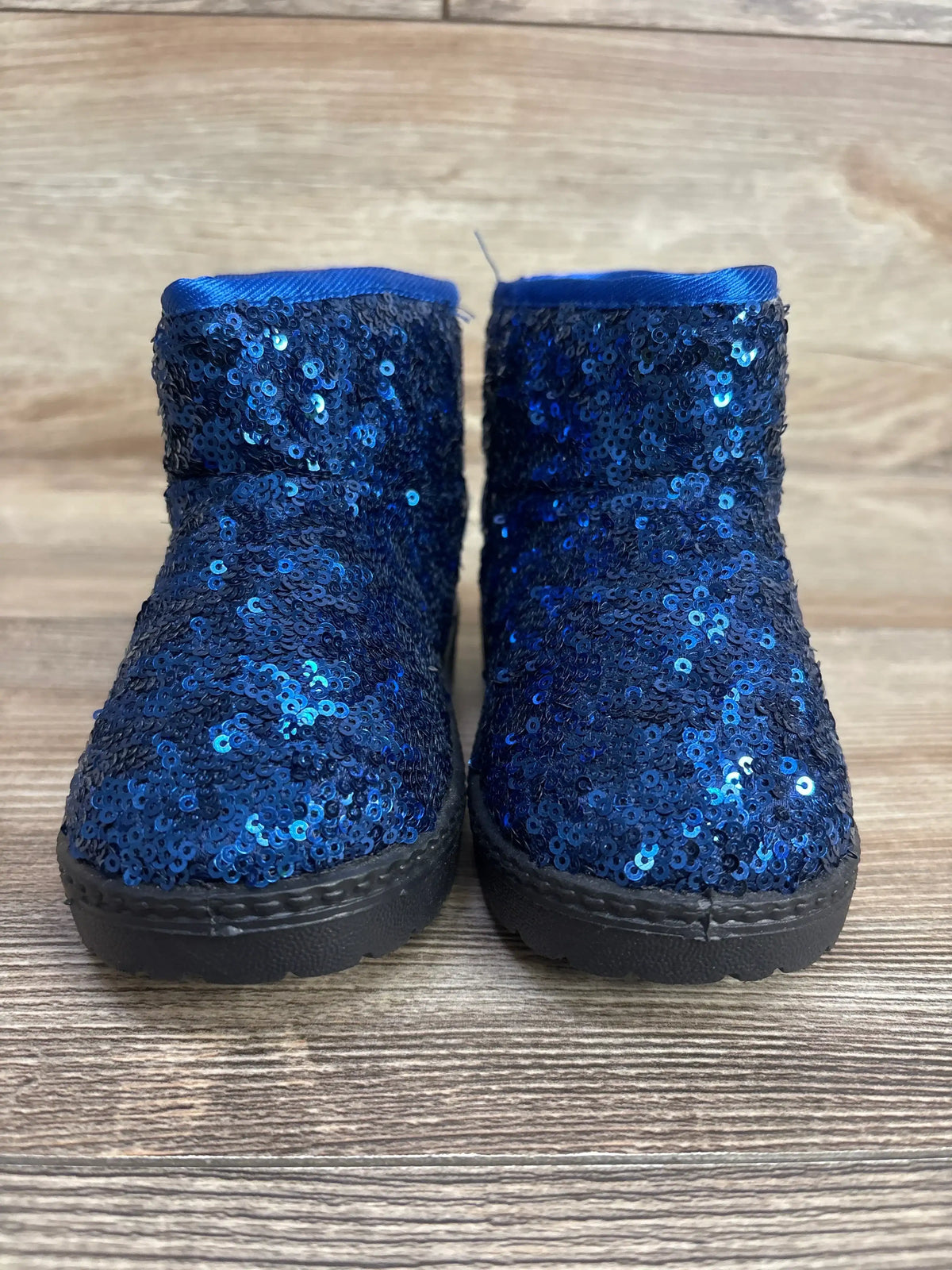 Pair of blue sequin toddler boots with black soles on wood background