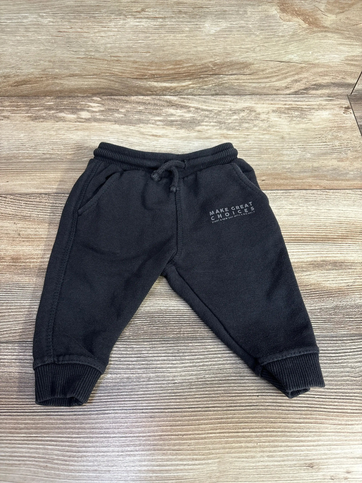 Black toddler sweatpants with ribbed cuffs and front pockets, featuring text 'Make Great Choices' on wooden floor