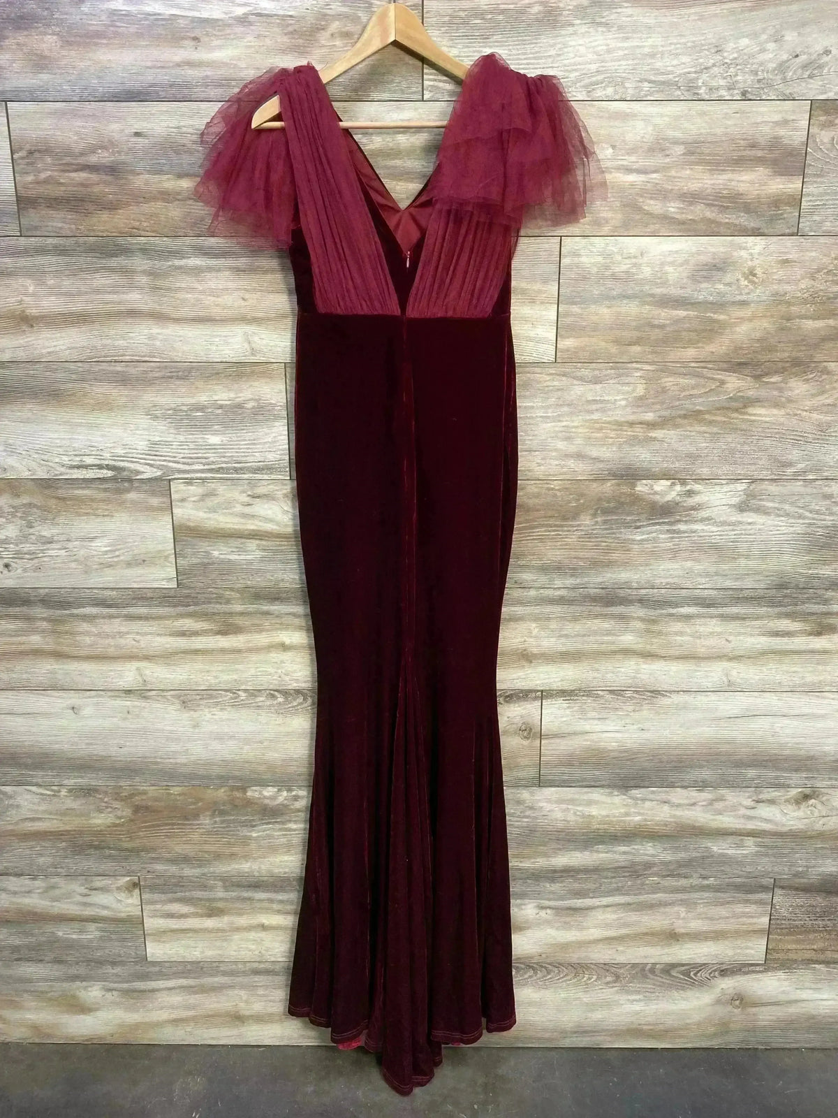 Front view of burgundy velvet maternity mermaid dress with V-neck and layered tulle shoulders on wood background